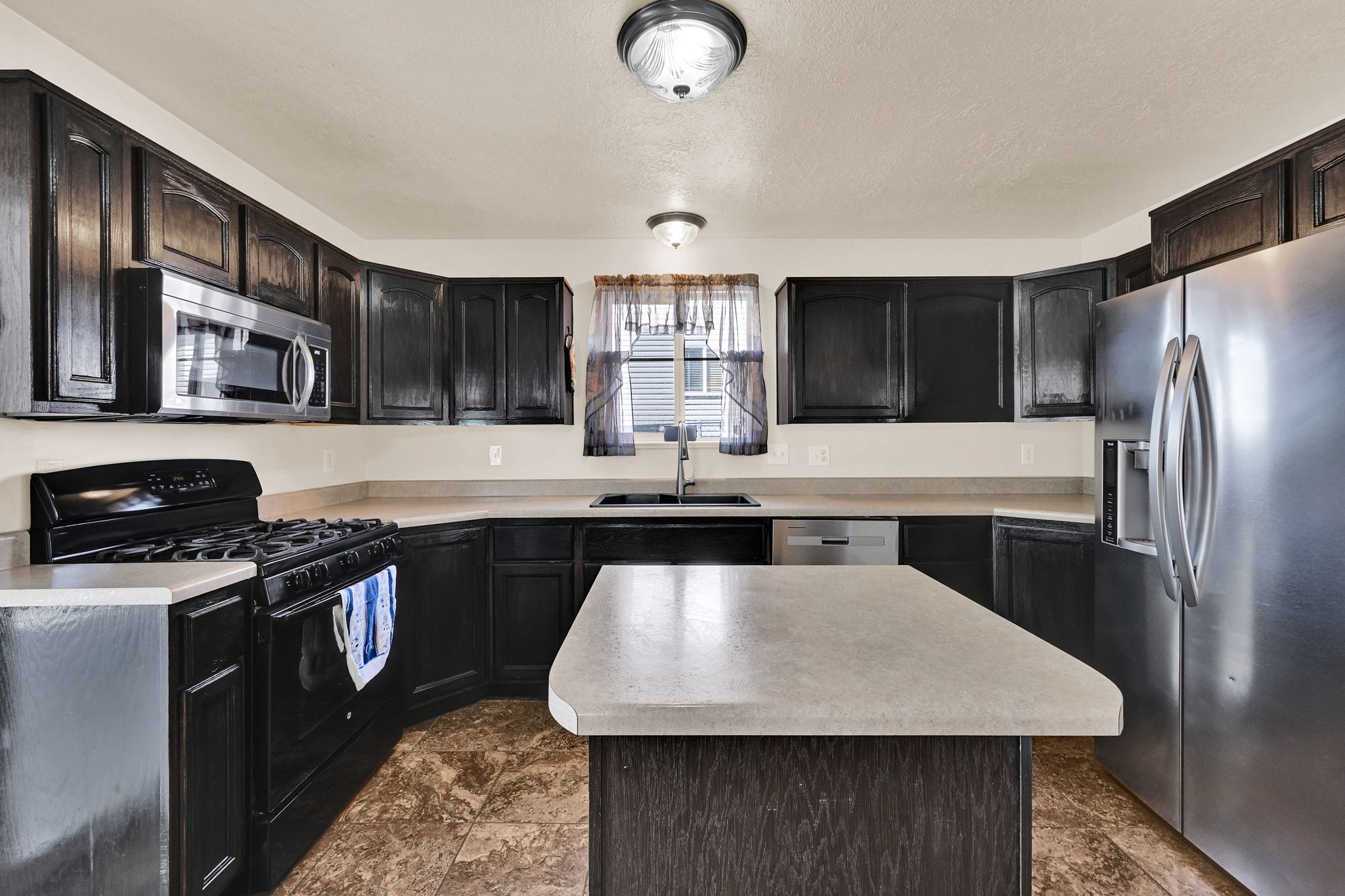 Kitchen featuring dark wood cabinetry, light-toned countertops, stainless steel appliances, and a central island