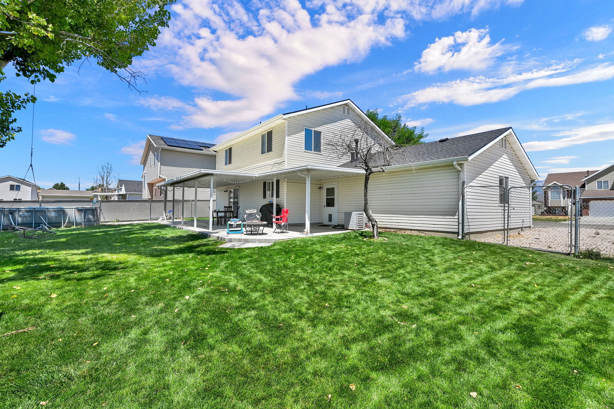 Spacious backyard featuring a large concrete patio, covered patio area, and expansive green lawn