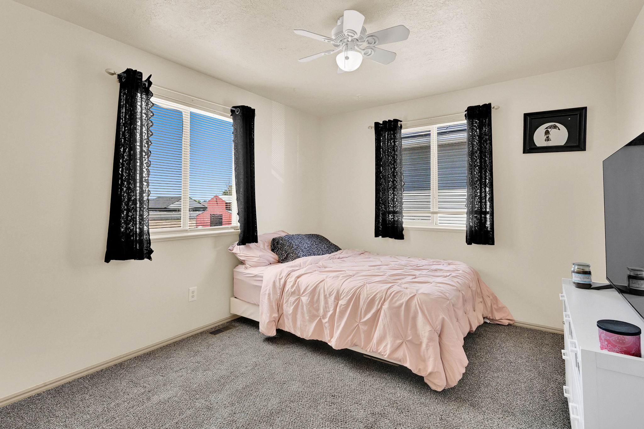 Carpeted room featuring two windows with horizontal blinds, a white ceiling fan with integrated lighting, and neutral wall tones