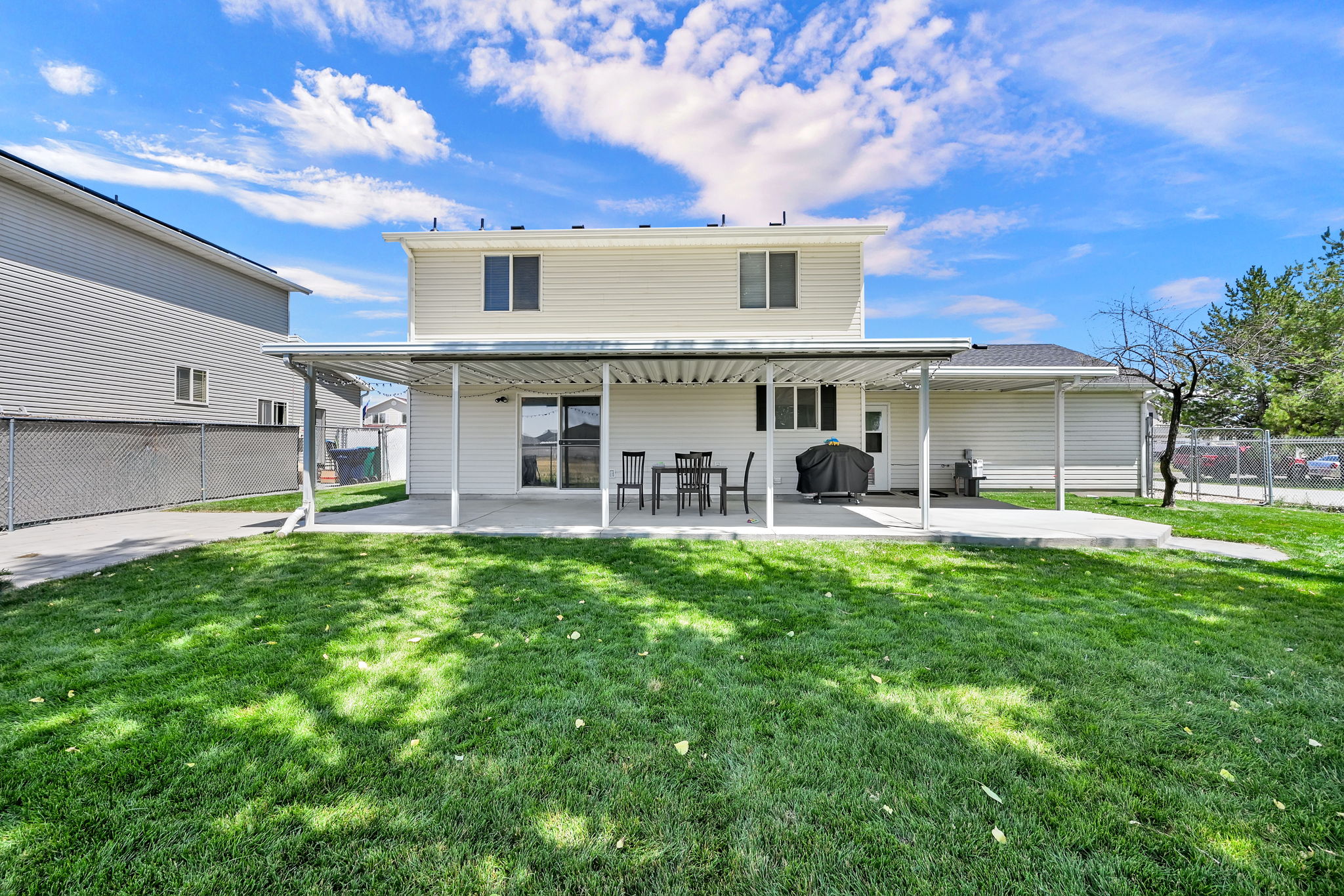 Expansive backyard with a manicured lawn, featuring a covered patio, concrete paving, and a chain-link fence