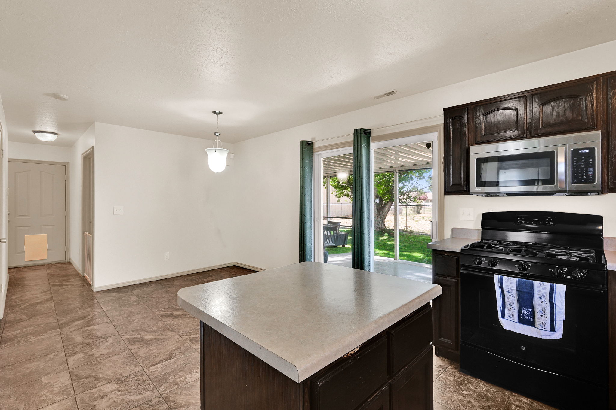 Kitchen featuring dark wood cabinetry, stainless steel microwave, black gas range, and light-toned countertops