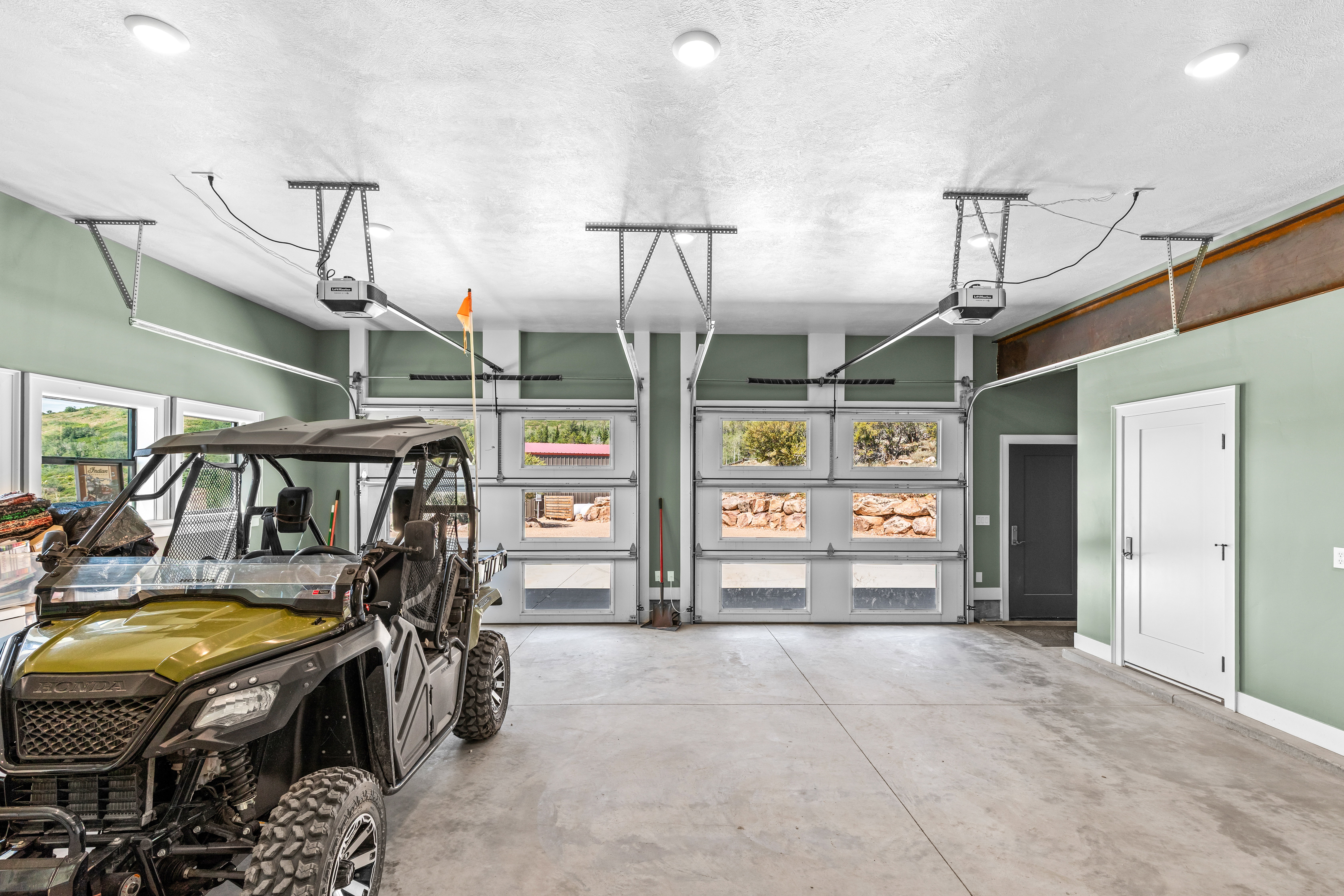 Spacious garage featuring a concrete floor, two overhead garage doors with frosted and clear glass panels, multiple recessed ceiling lights, and two interior doors