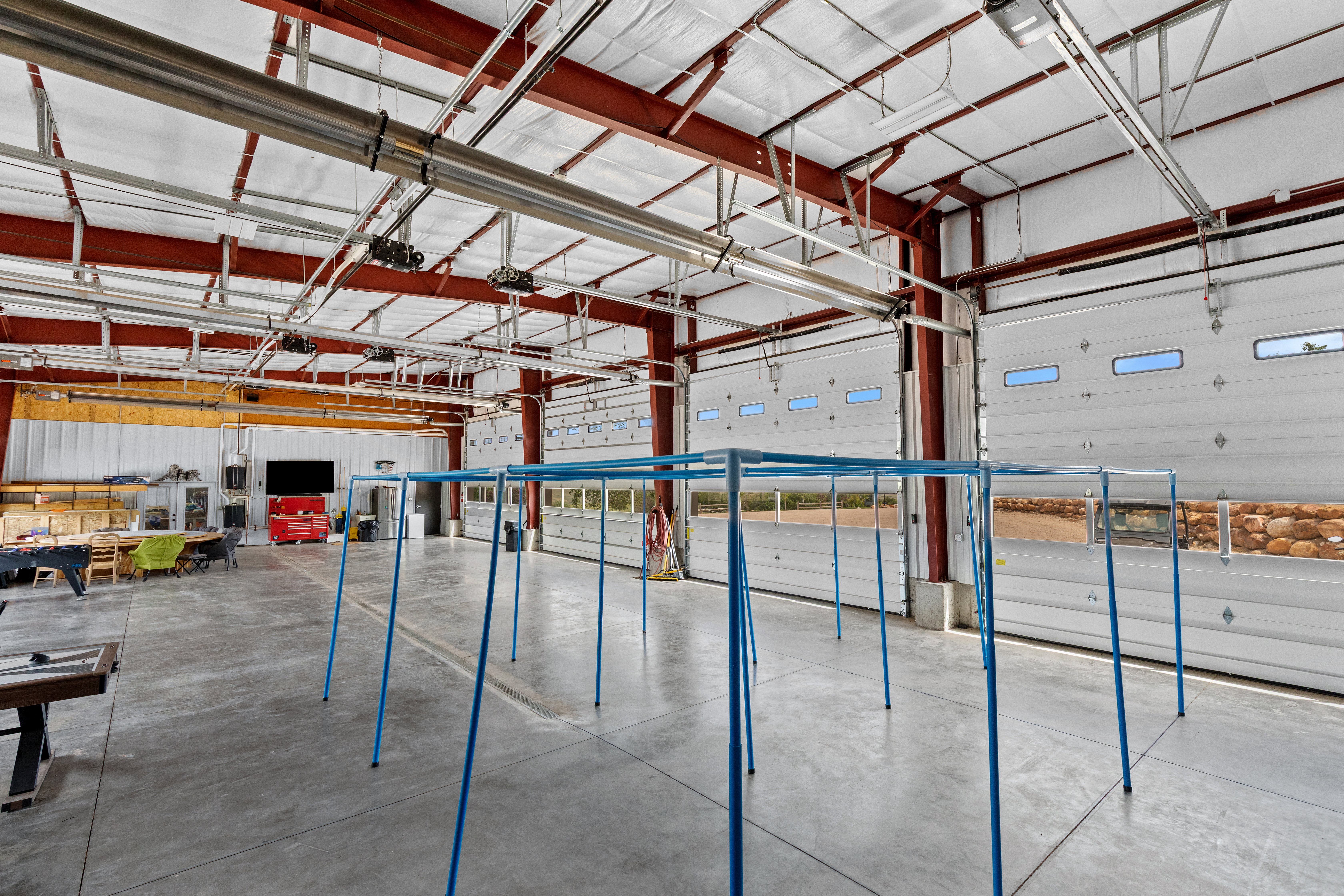Expansive commercial bay featuring a polished concrete floor, red I-beam construction, and multiple overhead doors with integrated windows