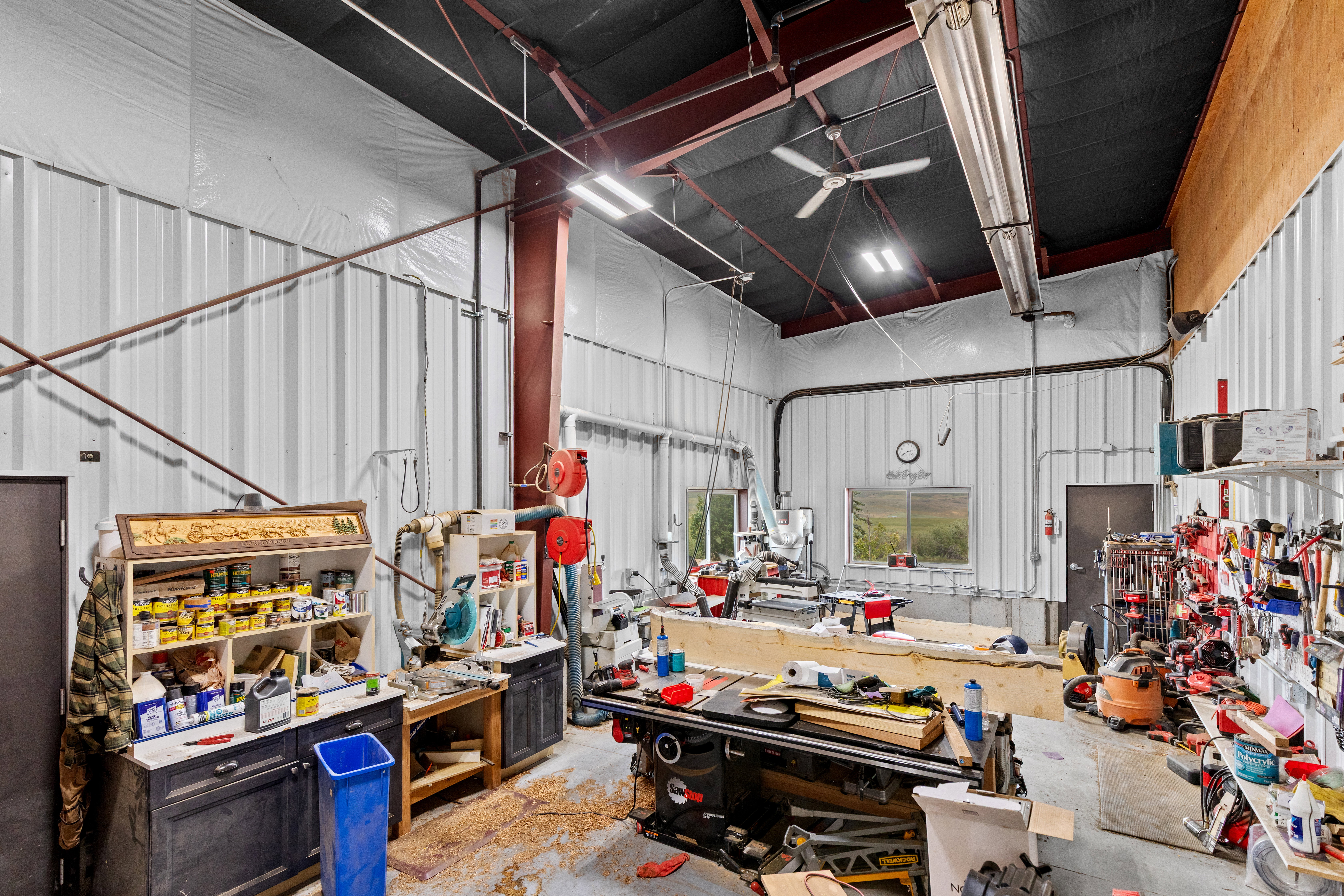 Spacious workshop featuring corrugated metal walls, exposed structural beams, and a high ceiling with overhead lighting