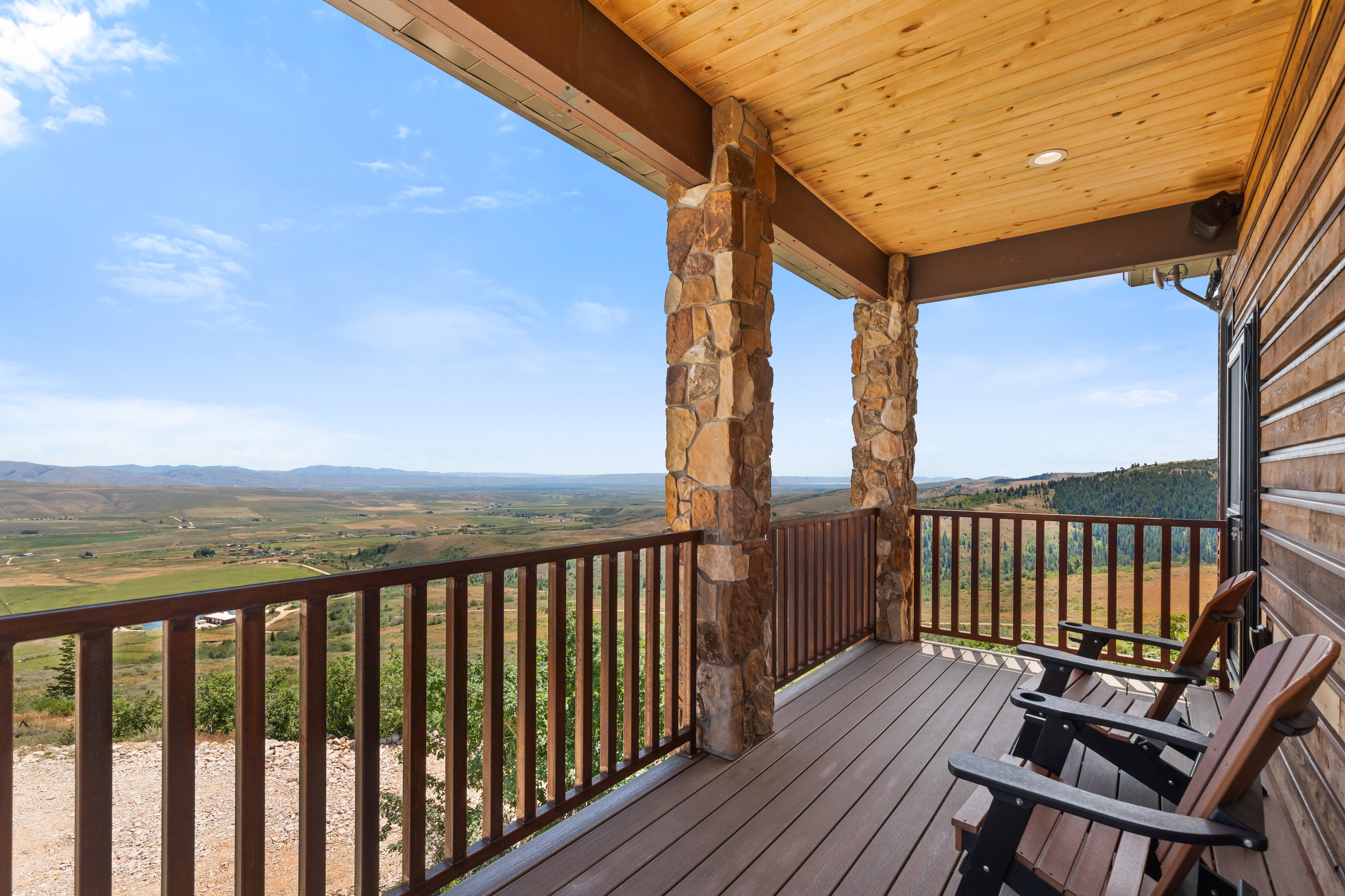 Covered deck featuring stone-clad pillars, wood-finish ceiling, and durable composite decking, overlooking expansive mountain and valley scenery