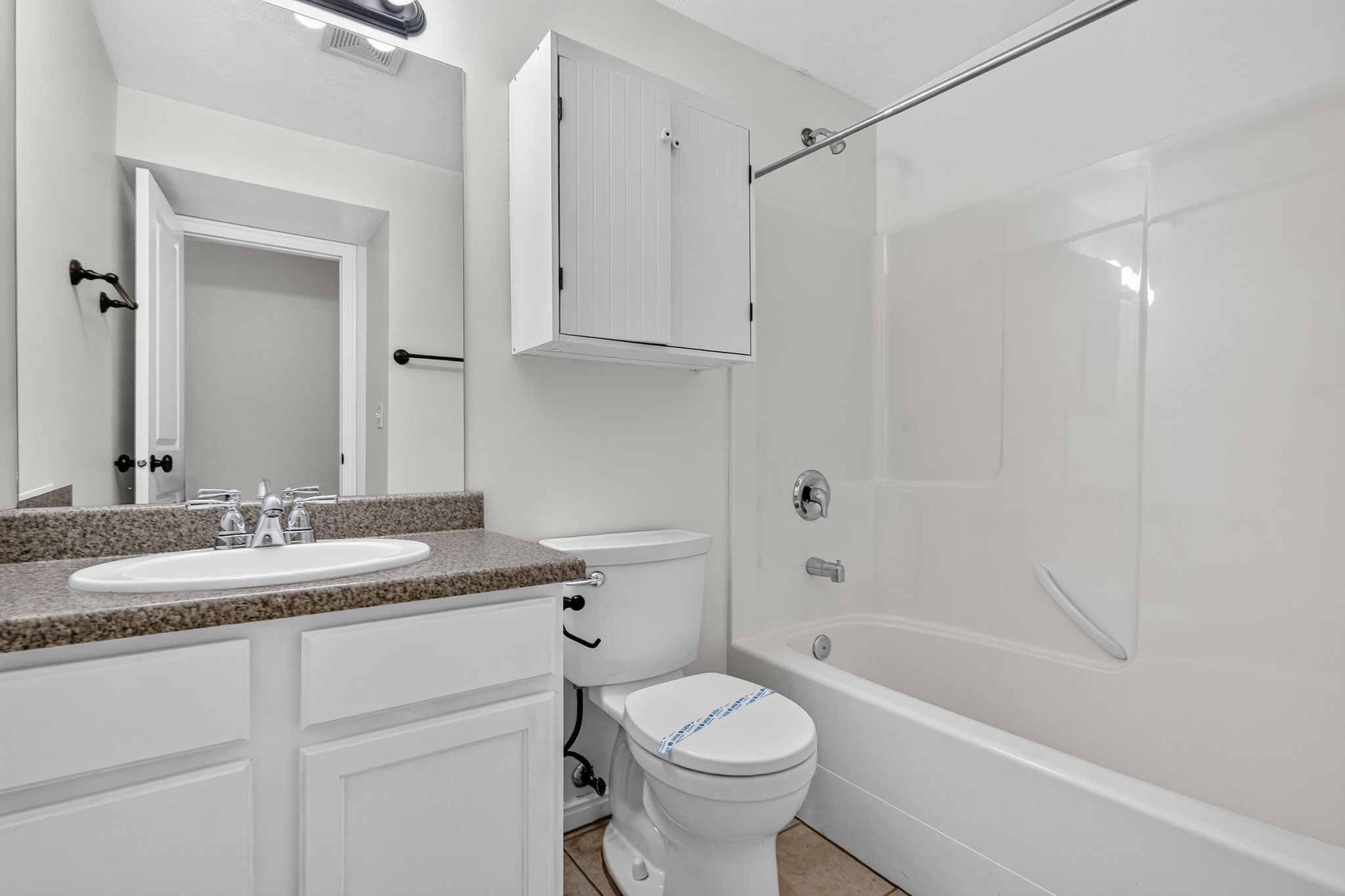 Bathroom featuring a white vanity with a speckled countertop, an integrated sink, a wall-mounted medicine cabinet, and a white tub/shower combination with chrome fixtures