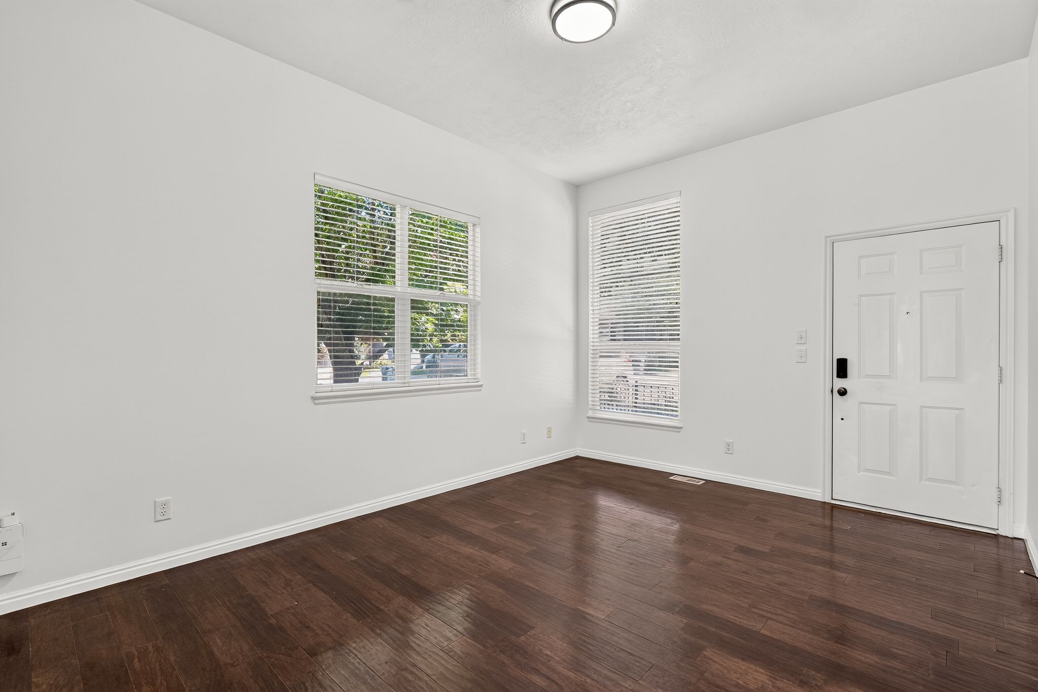 Spacious room featuring rich wood-finish flooring, white baseboards, and bright white walls