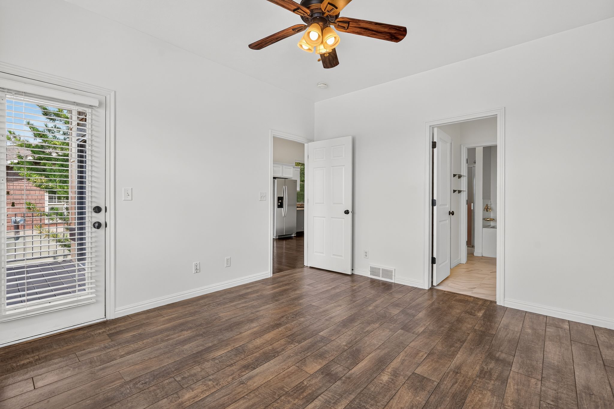 Spacious room featuring wood-finish flooring, white walls, and a ceiling fan with integrated lighting