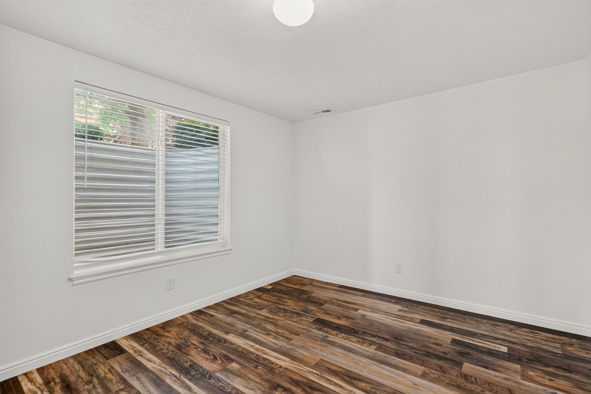 Bright room featuring wood-finish flooring, white baseboards, a single window with blinds, and clean white walls