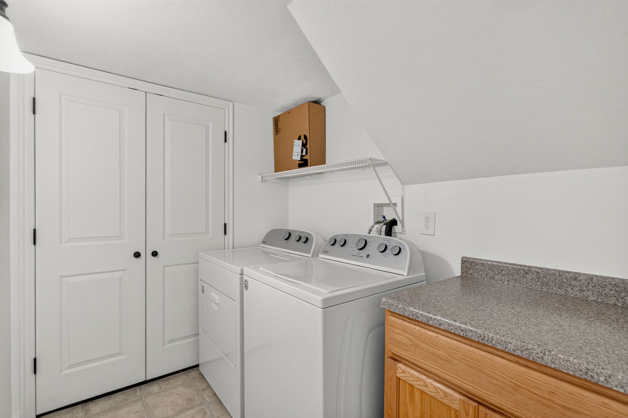 Dedicated laundry space featuring a tile floor, built-in shelving, and a solid-surface countertop with wood-finish cabinetry
