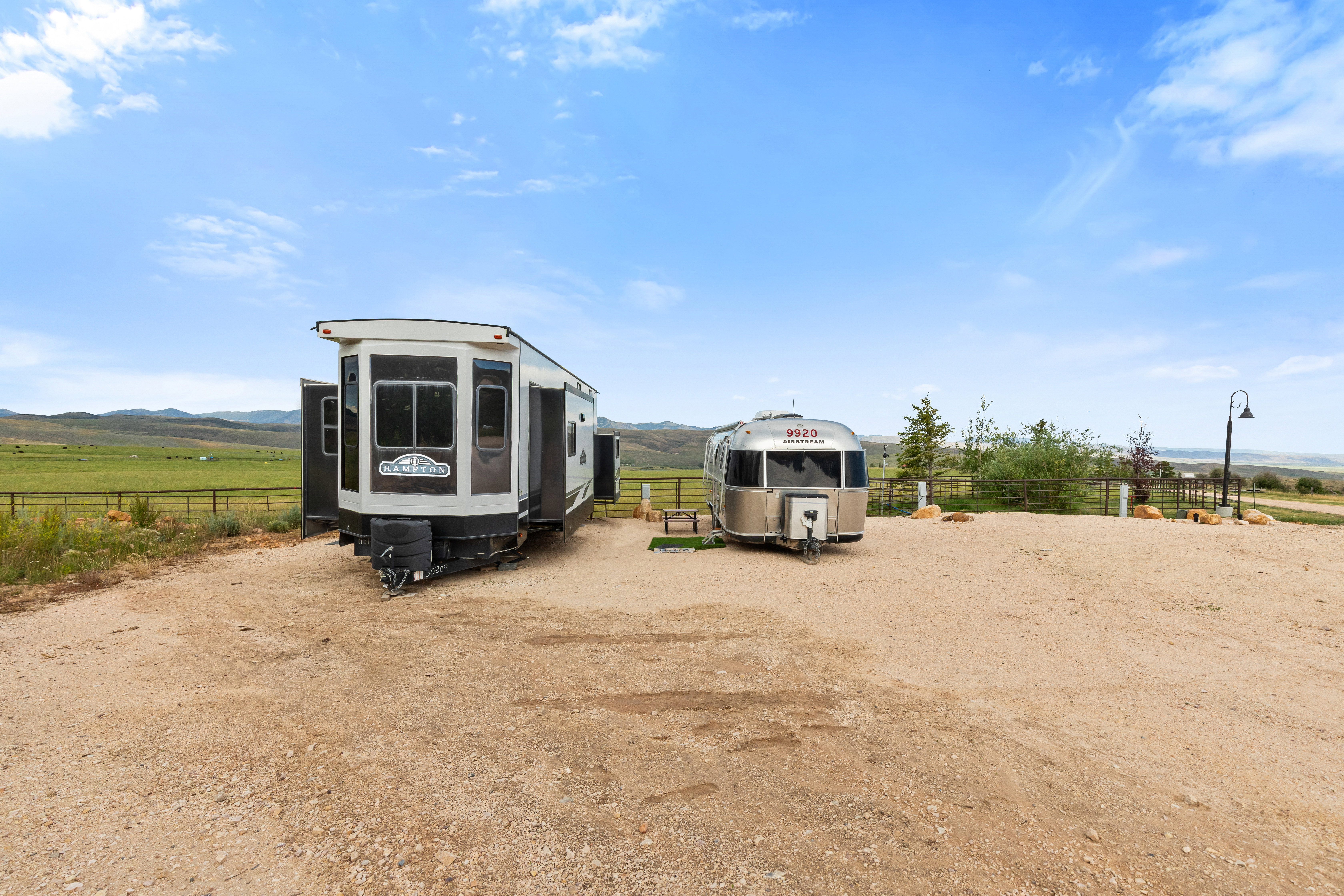 Gravel parking area featuring two recreational vehicles, a contemporary fifth-wheel trailer, and a classic Airstream trailer