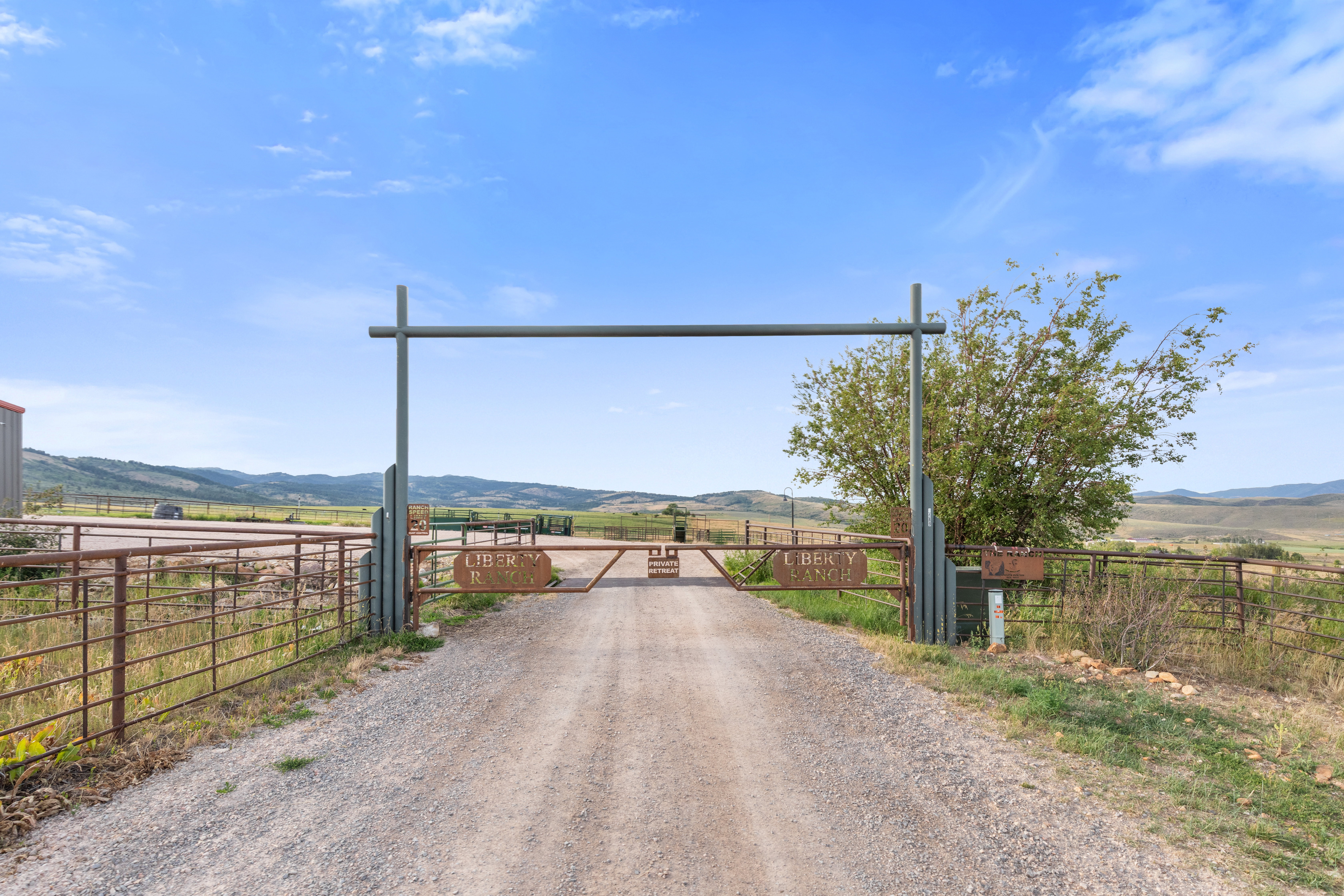 Gravel driveway entrance featuring a metal overhead gate structure and fencing