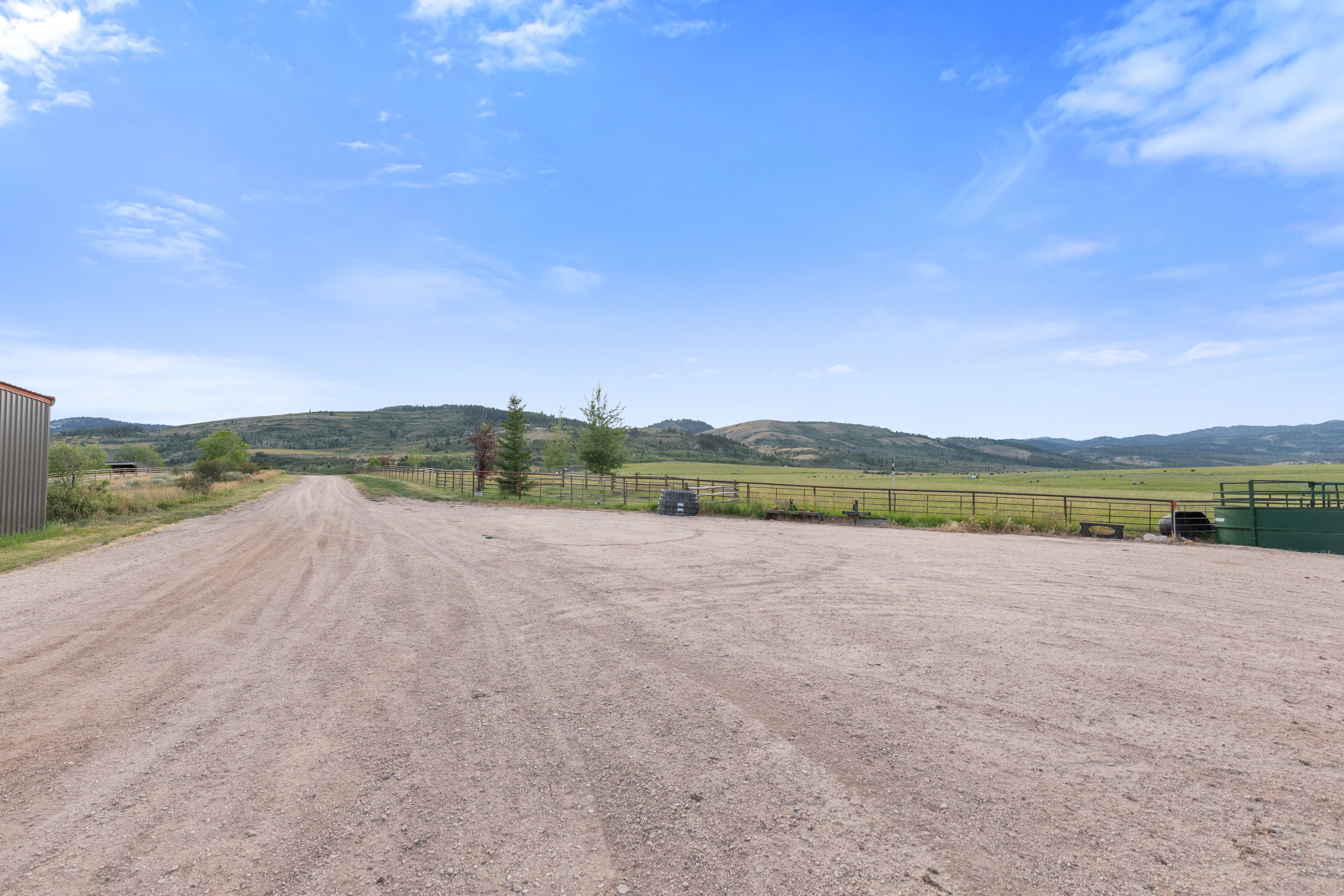 Expansive gravel driveway providing extensive parking and access to the property, bordered by a metal siding structure and fencing