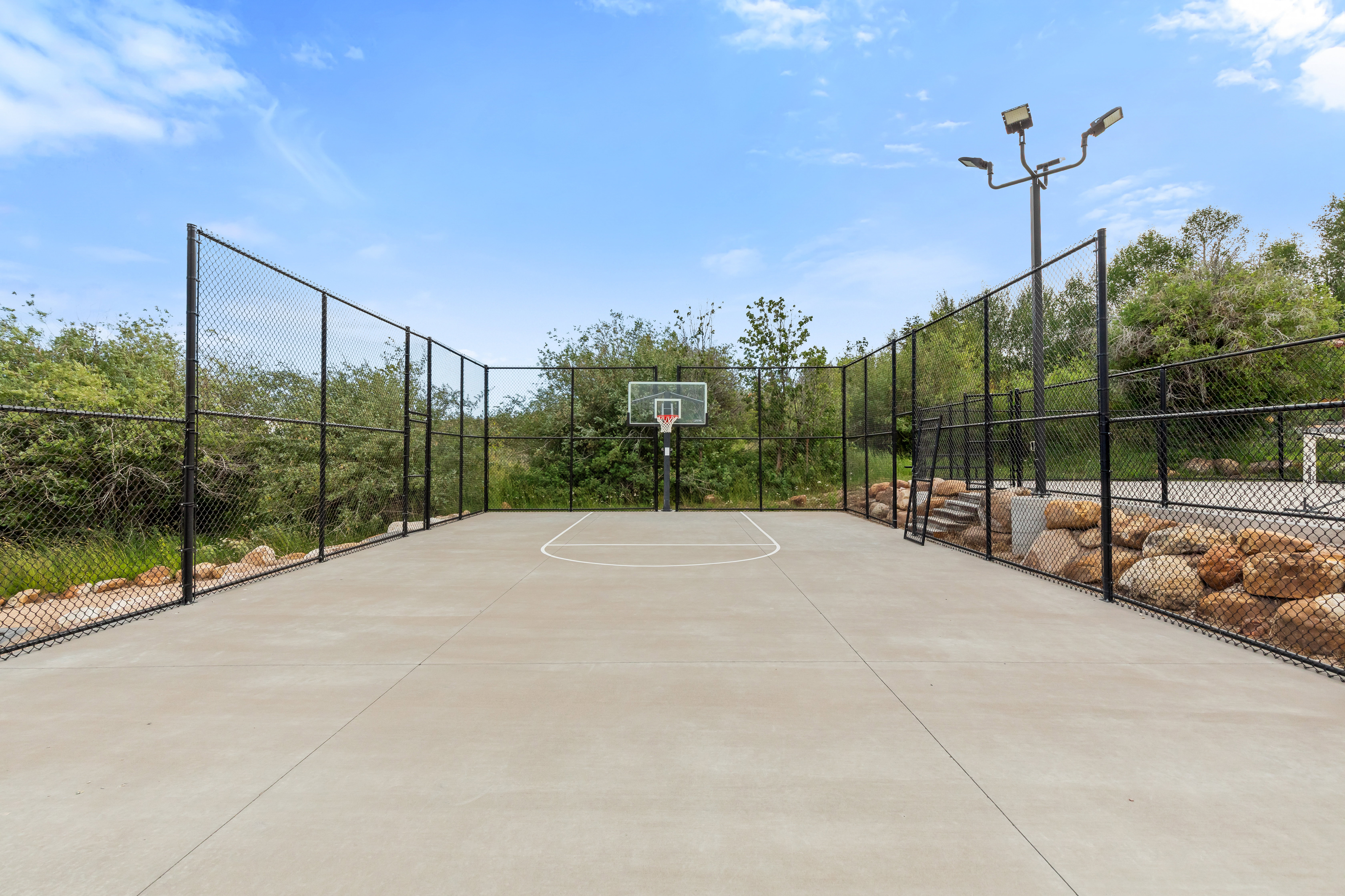 Private concrete sport court featuring an adjustable basketball hoop, perimeter fencing, and integrated lighting