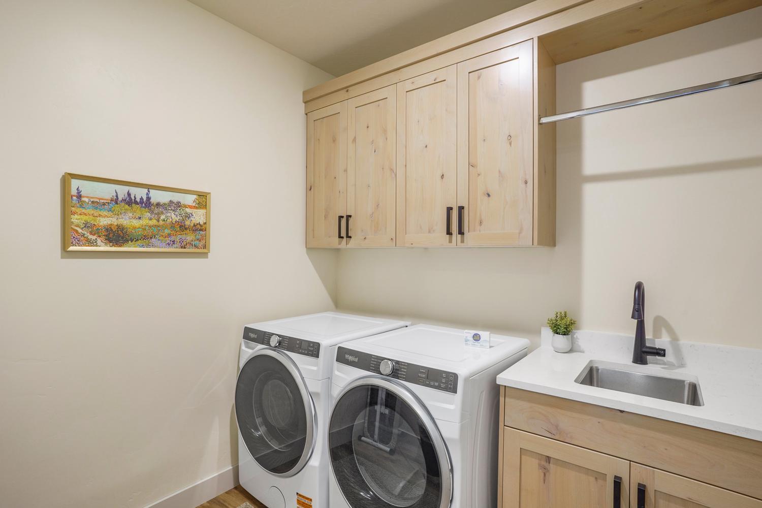 Laundry area featuring wood-finish cabinetry, a utility sink with a matte black faucet, and a hanging rod