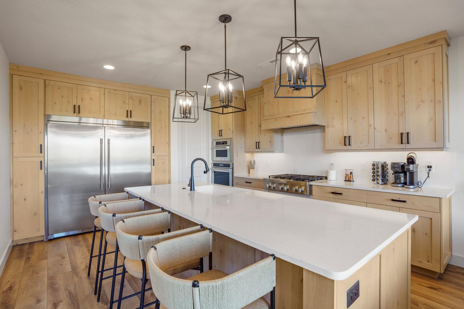 Kitchen featuring a large central island with a solid surface countertop, stainless steel refrigerator and range, wood-finish cabinetry, and contemporary pendant lighting