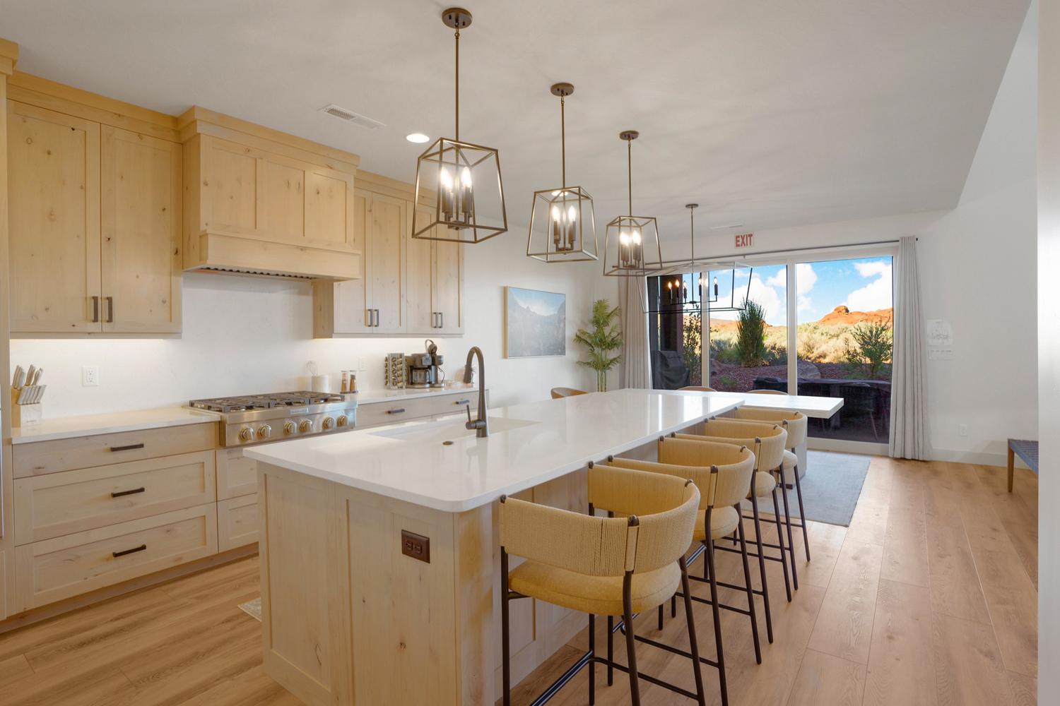 Spacious kitchen featuring light wood cabinetry, white countertops, a large center island with seating, stainless steel appliances, and wood-finish flooring