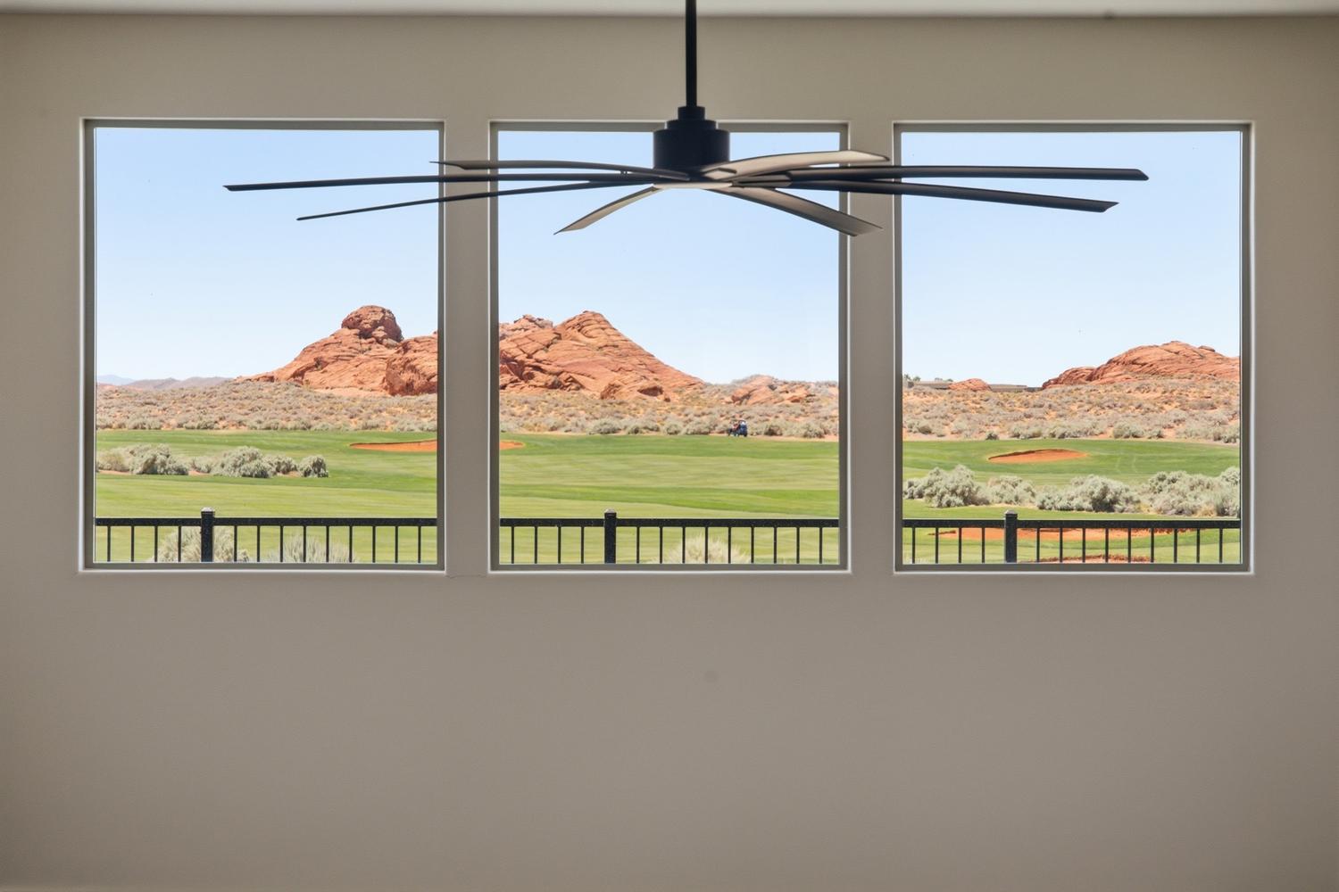 Three expansive windows frame a verdant golf course and distant red rock formations