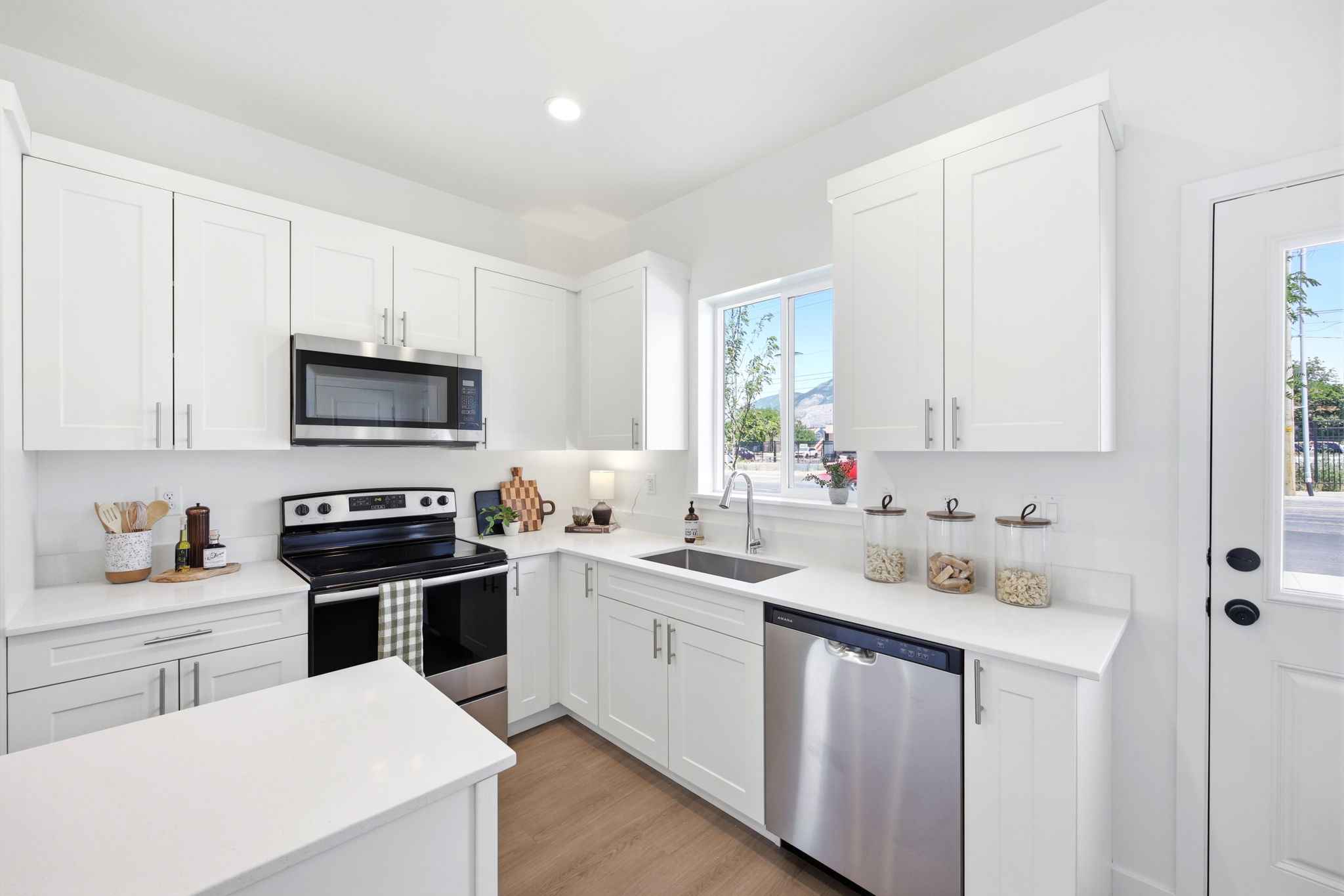 Modern kitchen featuring white shaker cabinetry, stainless steel appliances, a large window, and light wood-finish flooring