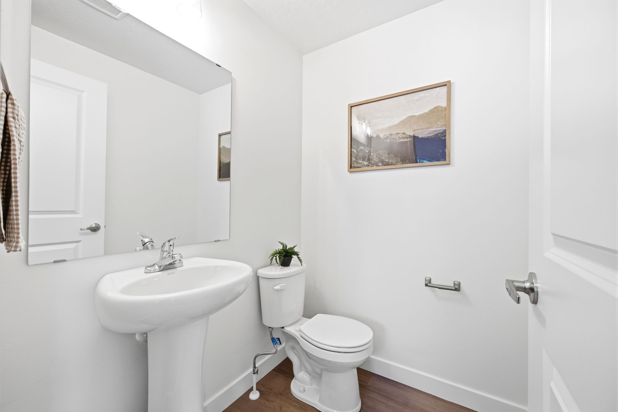 Pedestal sink with chrome faucet, large frameless mirror, and wood-finish flooring