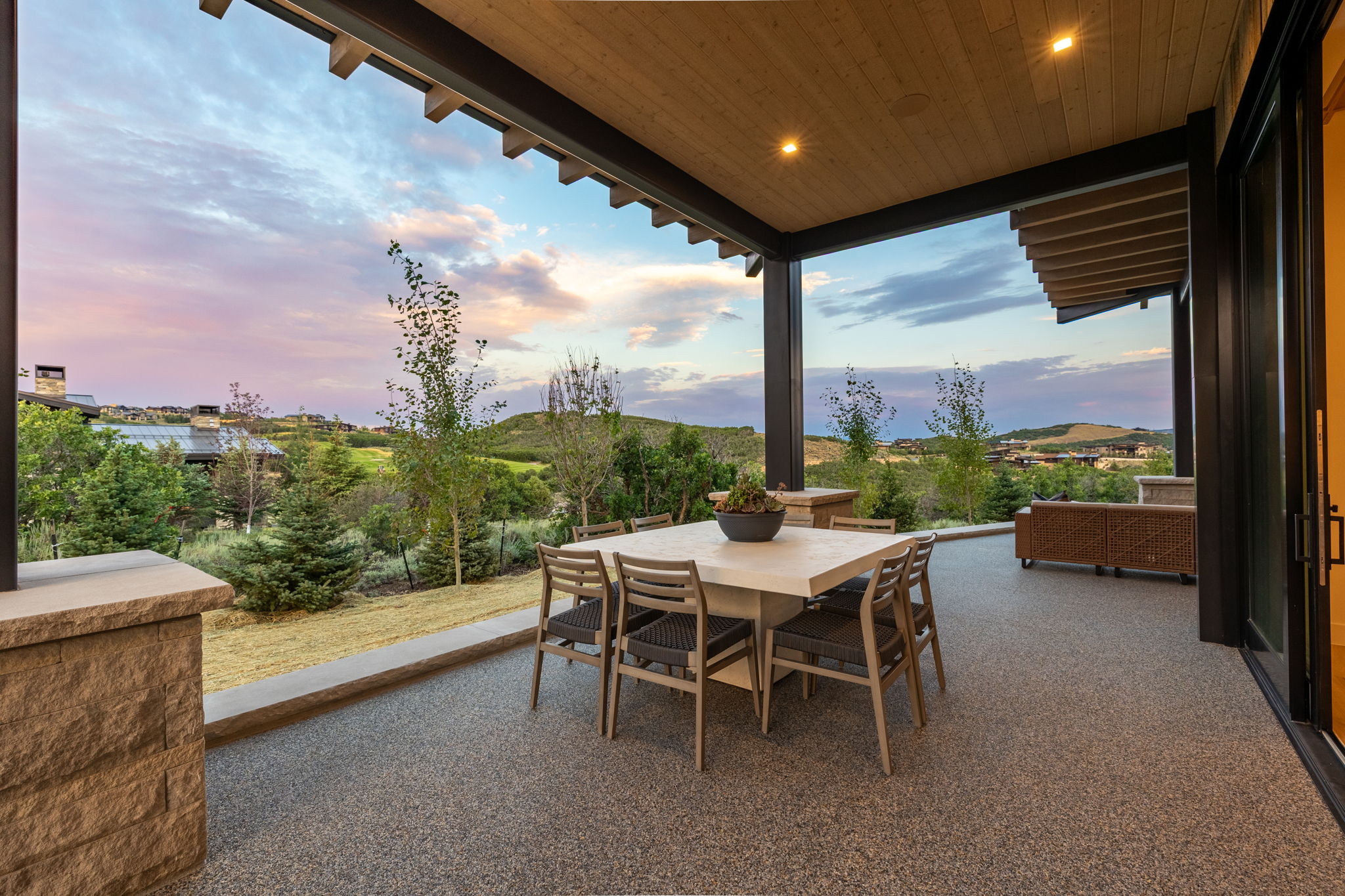 Spacious covered patio featuring a wood-panel ceiling with recessed lighting, exposed beams, and a textured aggregate floor