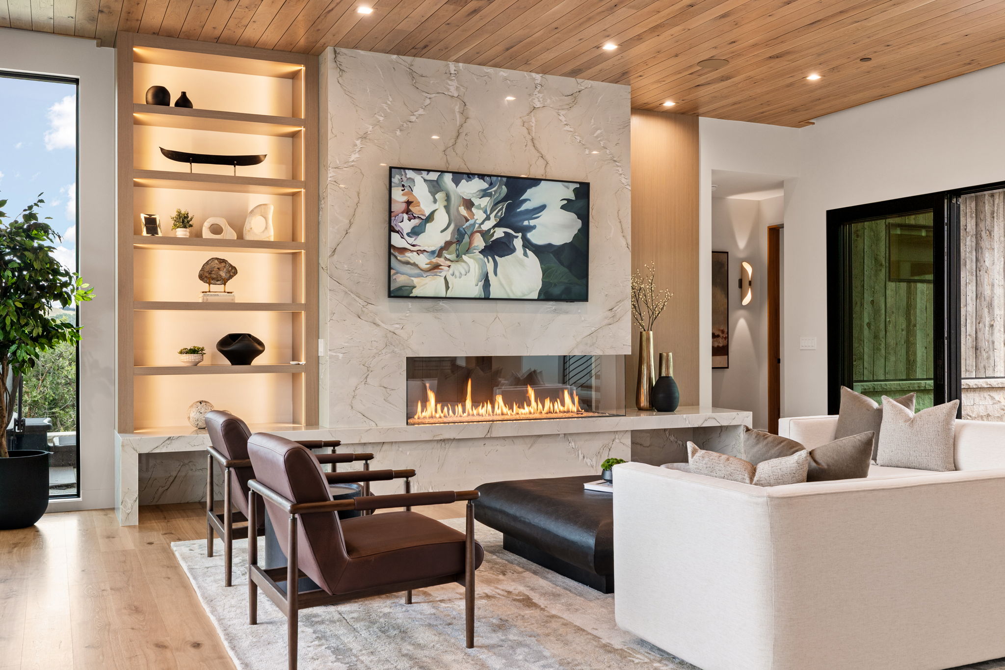 Living space featuring a natural wood-finish ceiling, a multi-sided linear fireplace with stone surround, recessed lighting, and built-in illuminated shelving