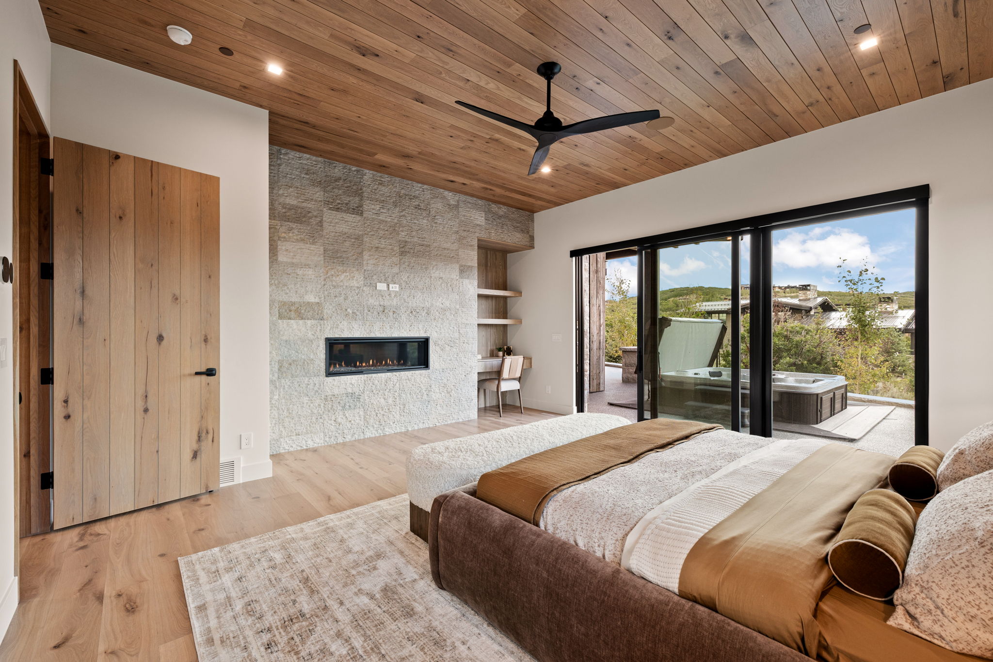 Bedroom featuring a wood-panel ceiling, stone accent wall with a linear fireplace, and wood-finish flooring