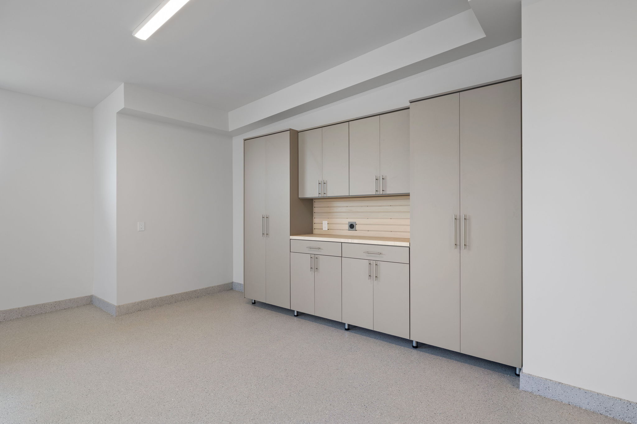 Garage featuring extensive built-in cabinetry, durable epoxy flooring, an integrated workbench, overhead lighting, and abundant storage