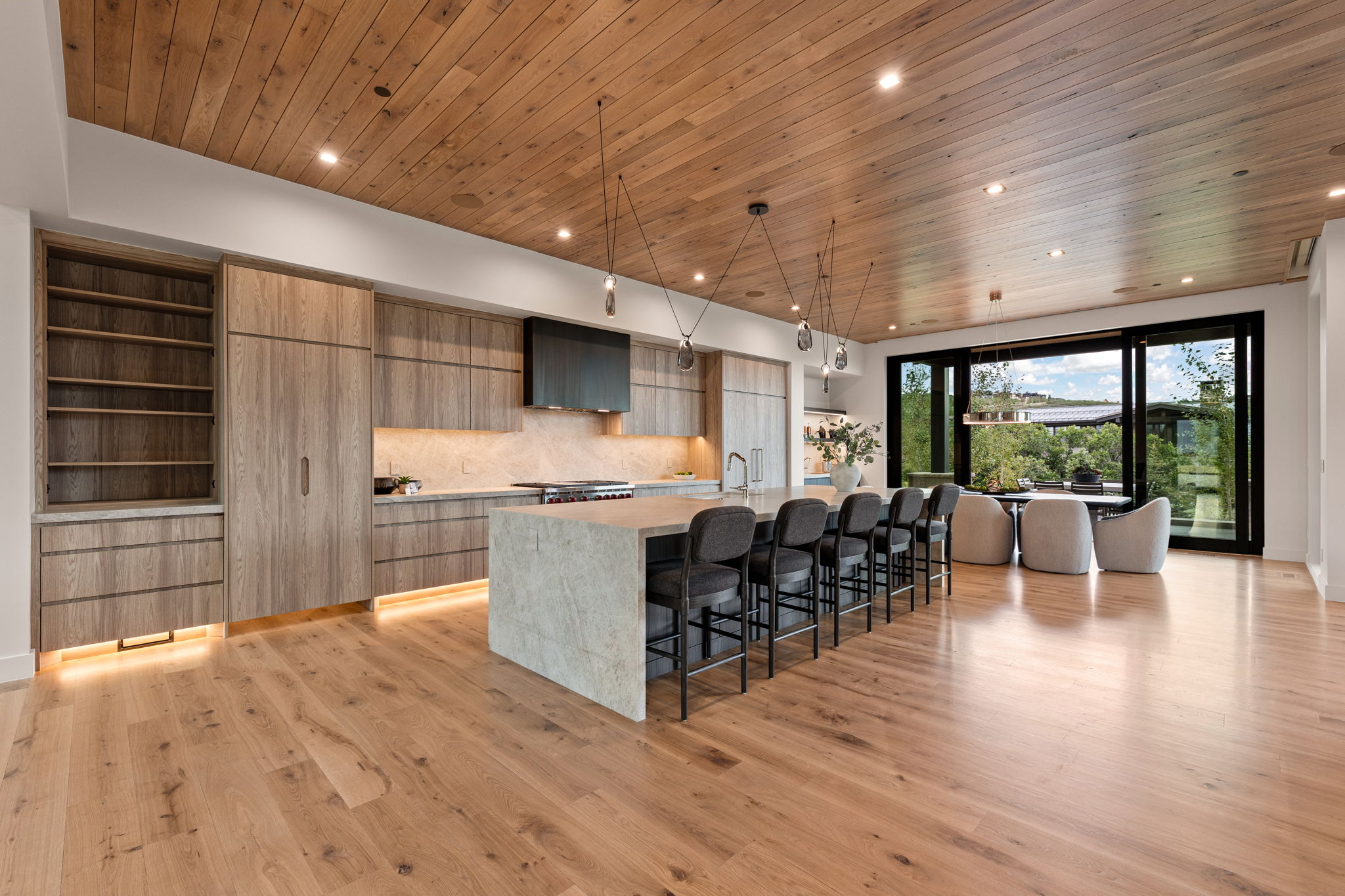 Open-concept kitchen and dining area featuring wood-finish flooring, a wood-paneled ceiling, and a large kitchen island with integrated seating