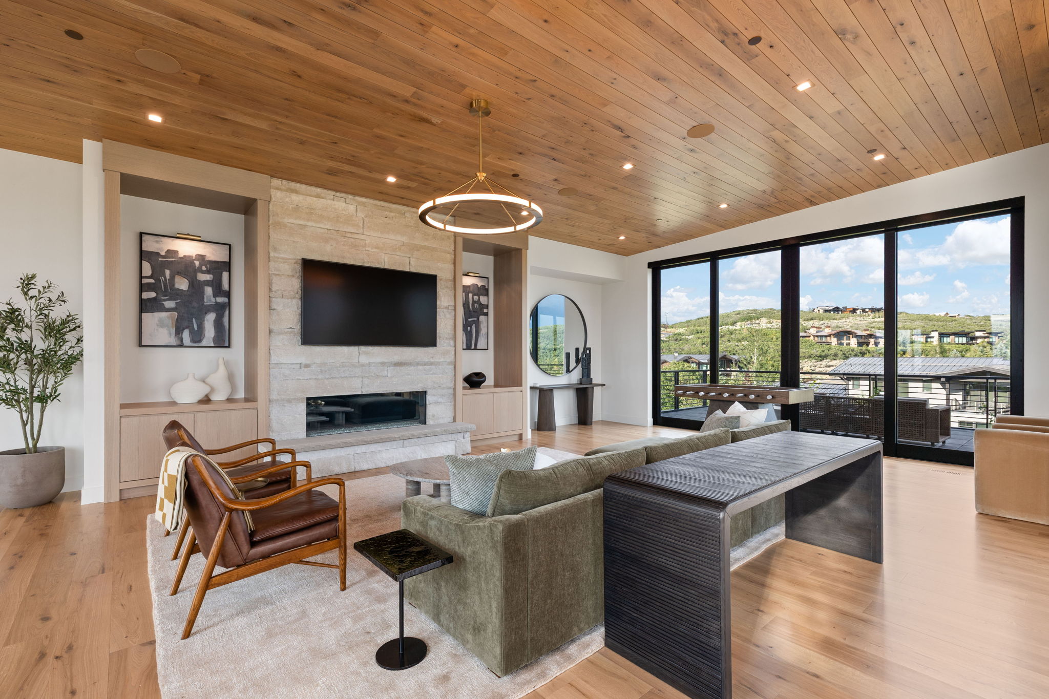 Spacious living area featuring a wood-panel ceiling, light wood-finish flooring, and a stone-clad fireplace with a linear insert