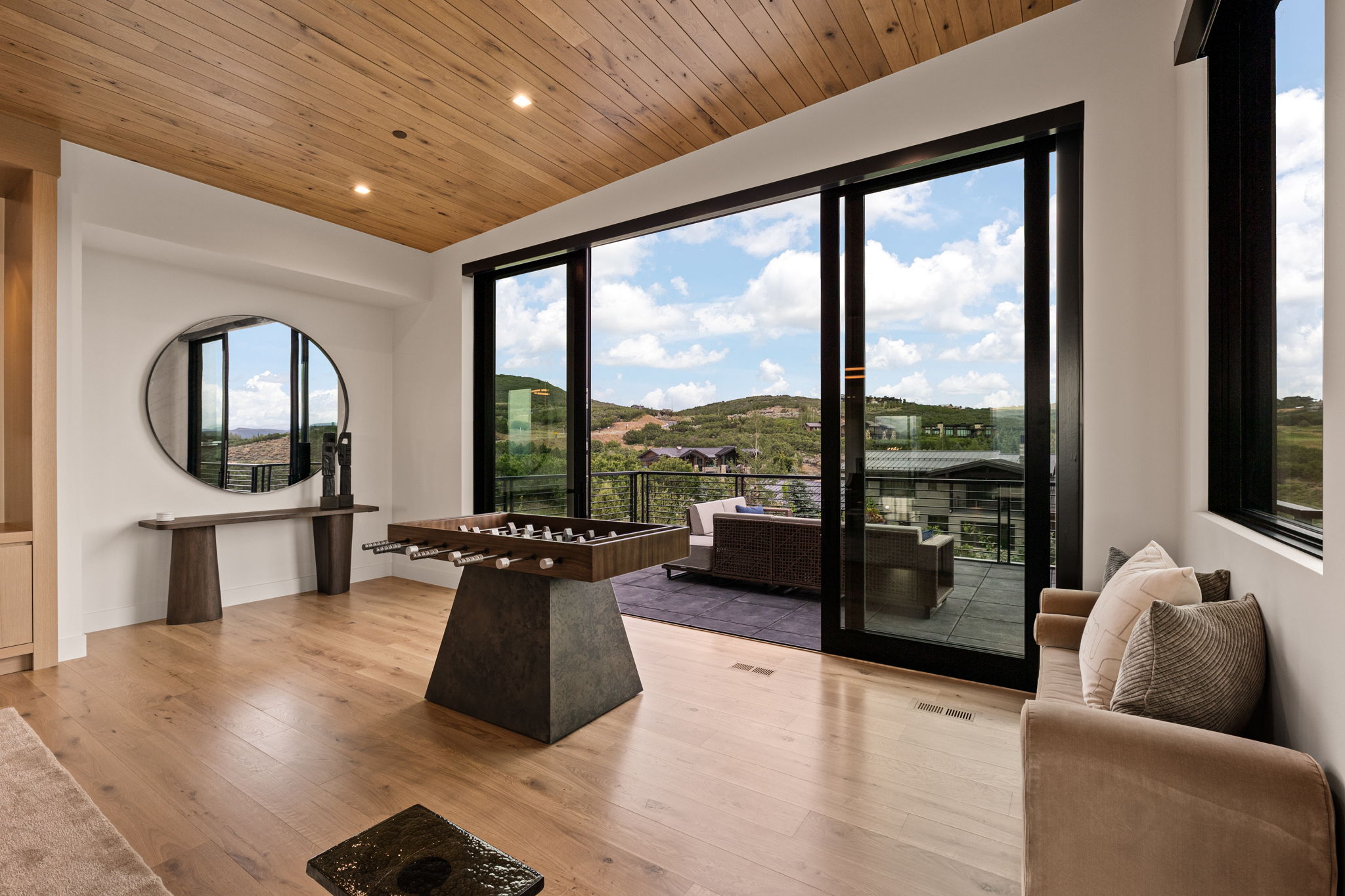 Spacious room featuring a wood-finish ceiling, light wood-finish flooring, and large sliding glass doors opening to an outdoor patio