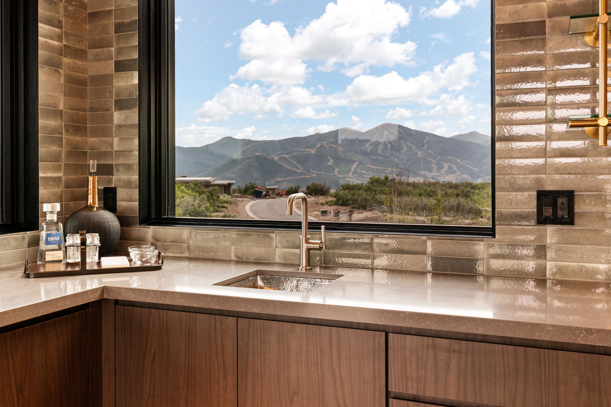 Corner wet bar featuring wood-finish cabinetry, a stone countertop, and a stainless steel undermount sink