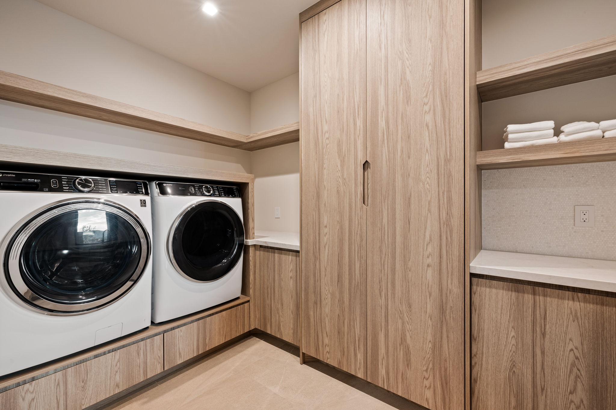 Utility room with wood-finish cabinetry, integrated washer and dryer, open shelving, and a light-toned countertop