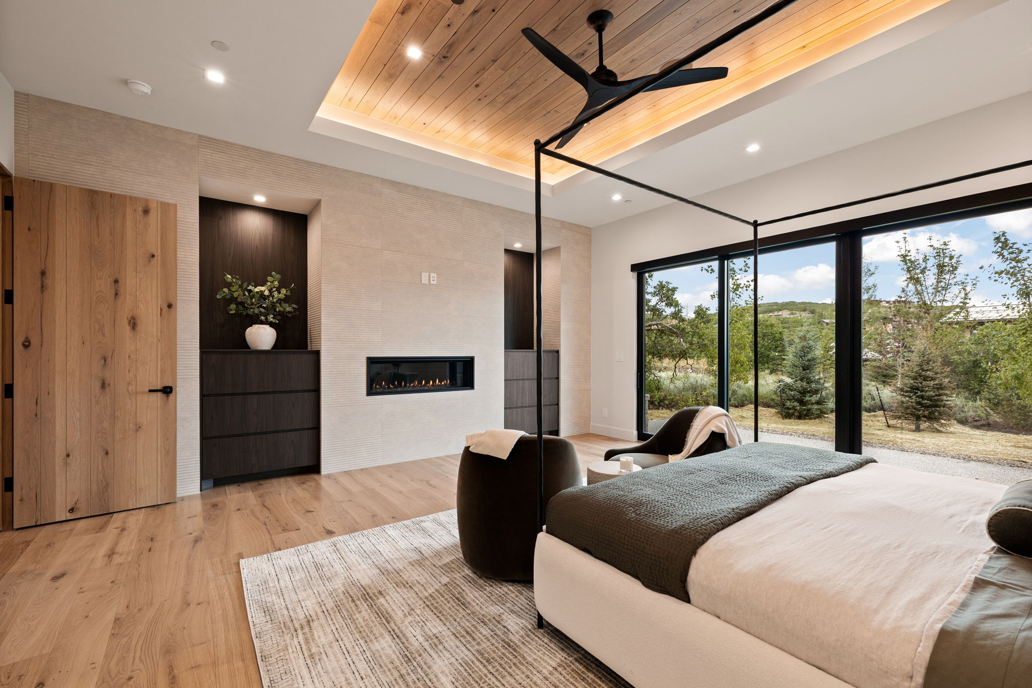 Spacious room featuring wood-finish flooring, a built-in linear fireplace, a wood-paneled ceiling with recessed lighting, and expansive glass doors opening to outdoor scenery