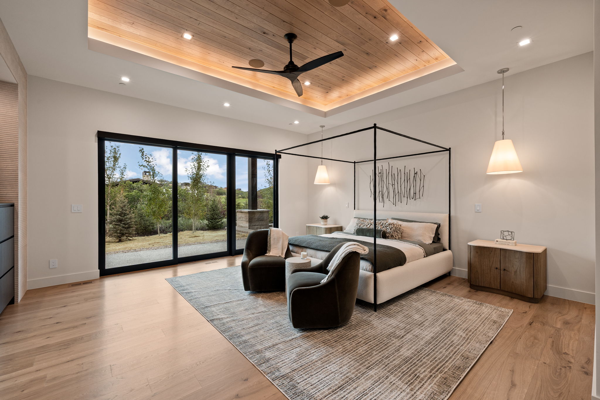 Spacious room featuring wood-finish flooring, a tray ceiling with wood paneling and recessed lighting, and a contemporary ceiling fan