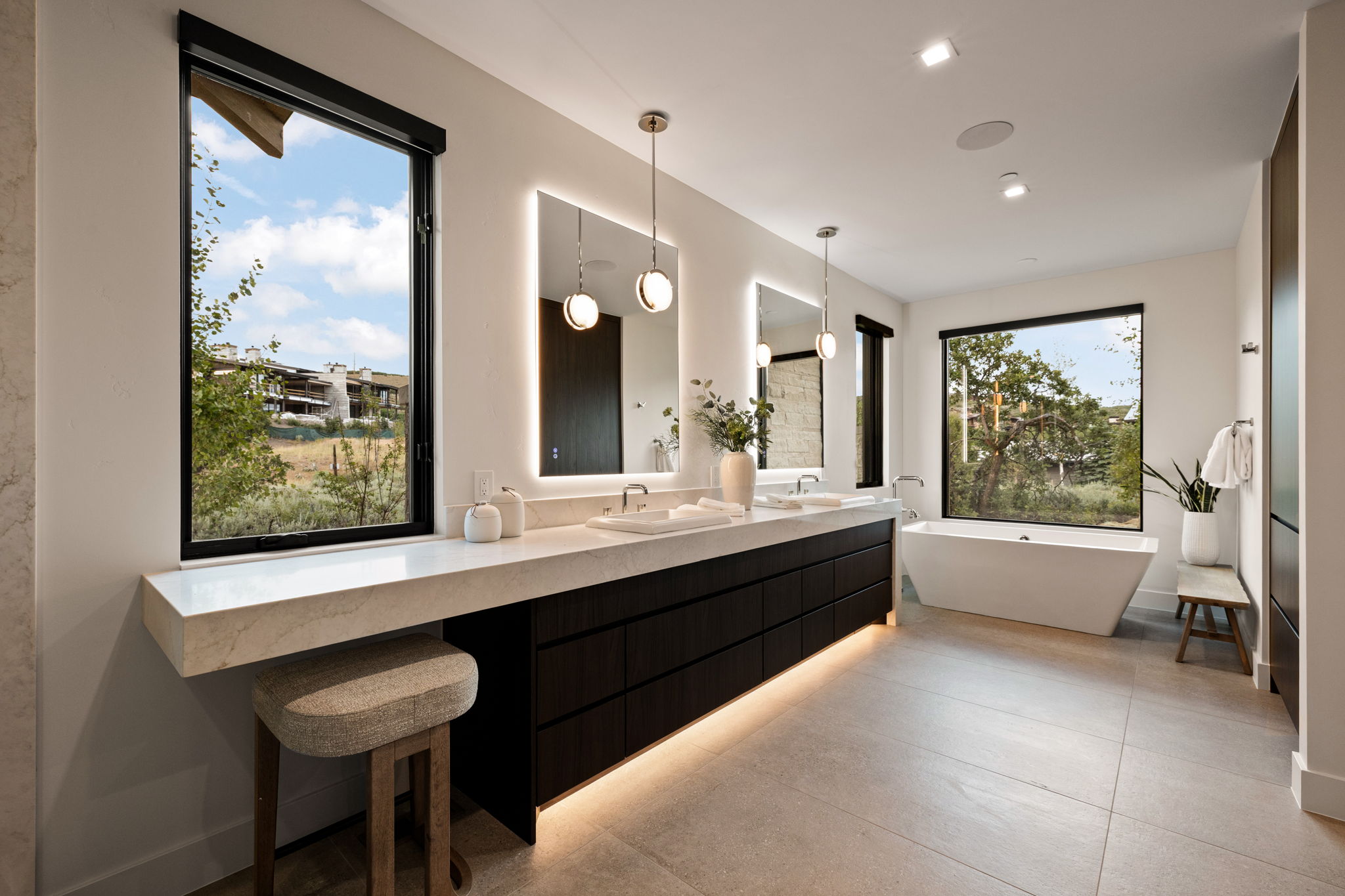 Spacious bathroom featuring a freestanding soaking tub, a long double vanity with integrated sinks, and ample natural light from multiple large windows