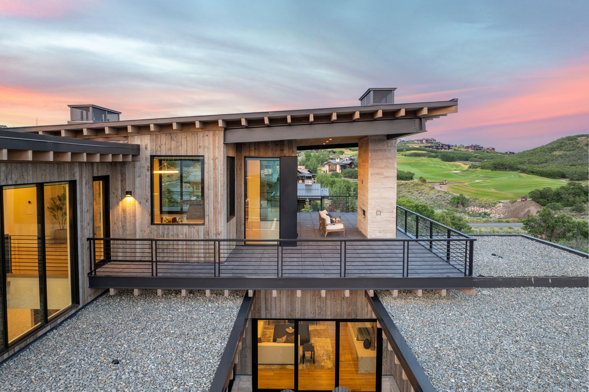 Multi-level dwelling with a wood-clad exterior, extensive fenestration, and an upper-level balcony featuring metal railings