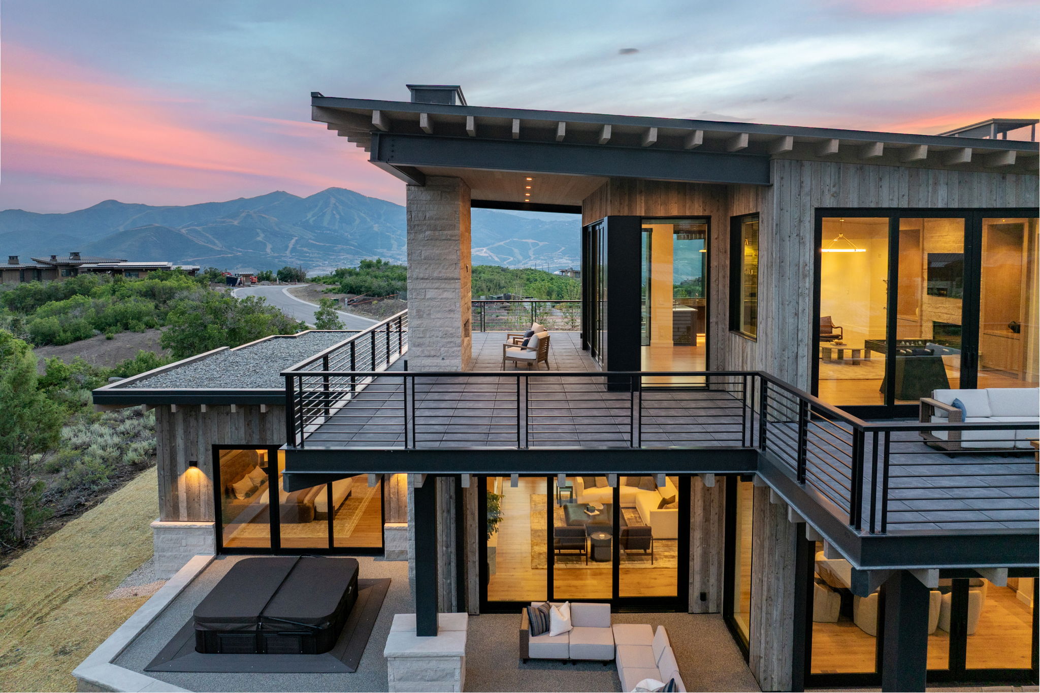 Multi-level modern residence featuring extensive decking, large format sliding glass doors, a stone hot tub surround, exterior wood paneling, and a flat roof design