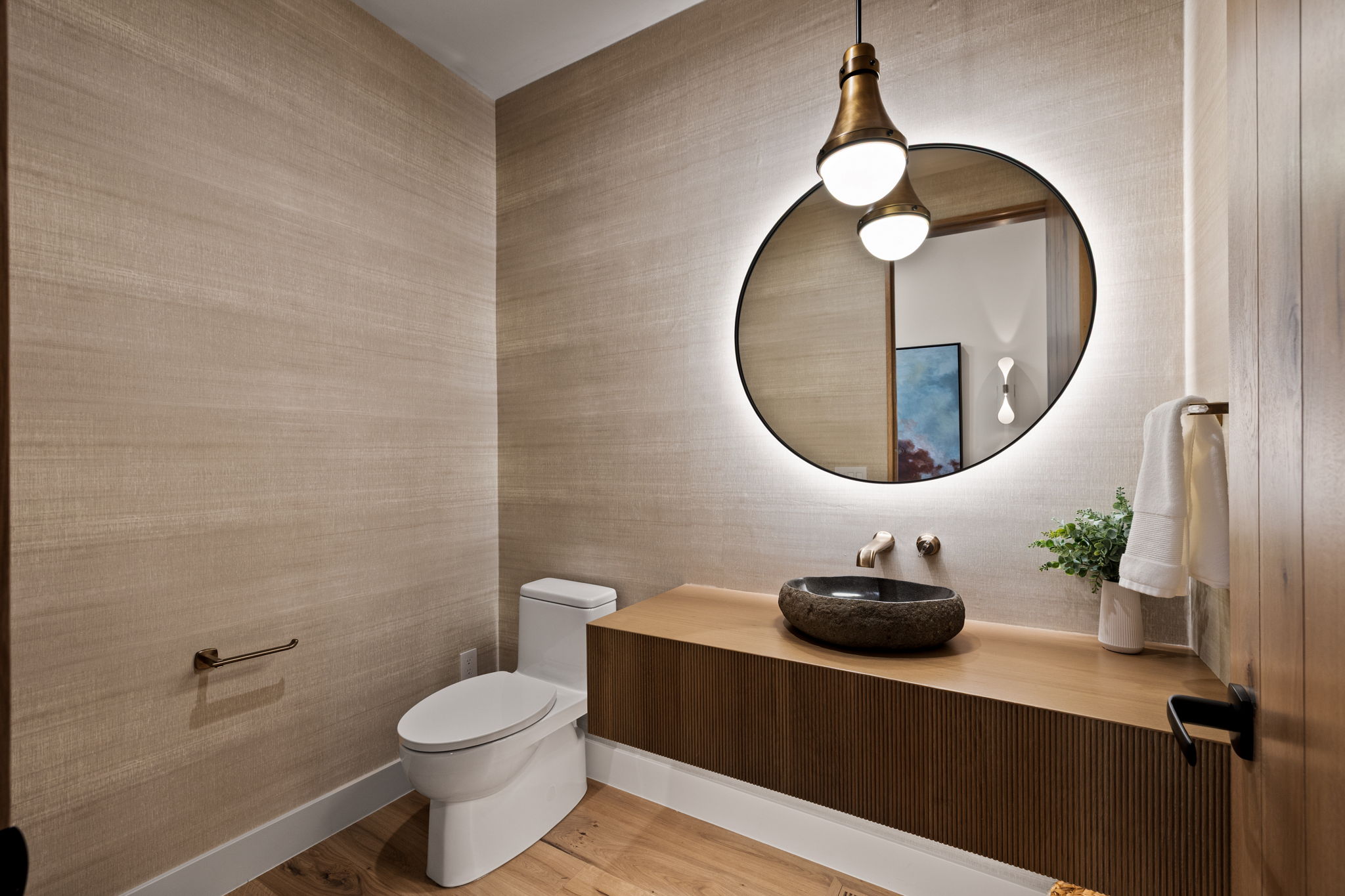 Powder room featuring wood-finish flooring, a contemporary vanity with a stone vessel sink, and an illuminated irregular-shaped mirror