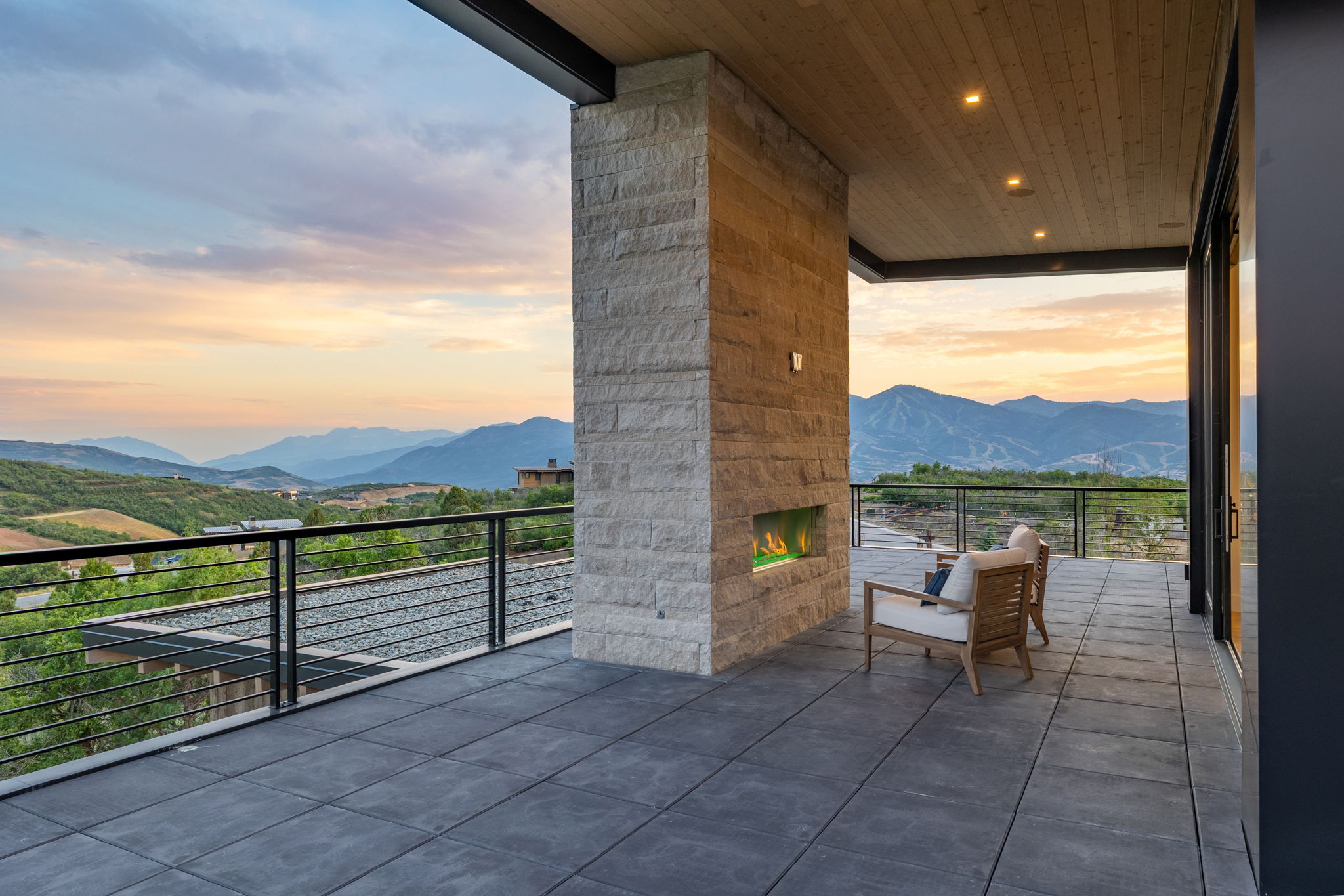 Expansive outdoor patio featuring large format tile flooring, a stone-clad fireplace with an integrated linear firebox, and a wood-paneled ceiling with recessed lighting
