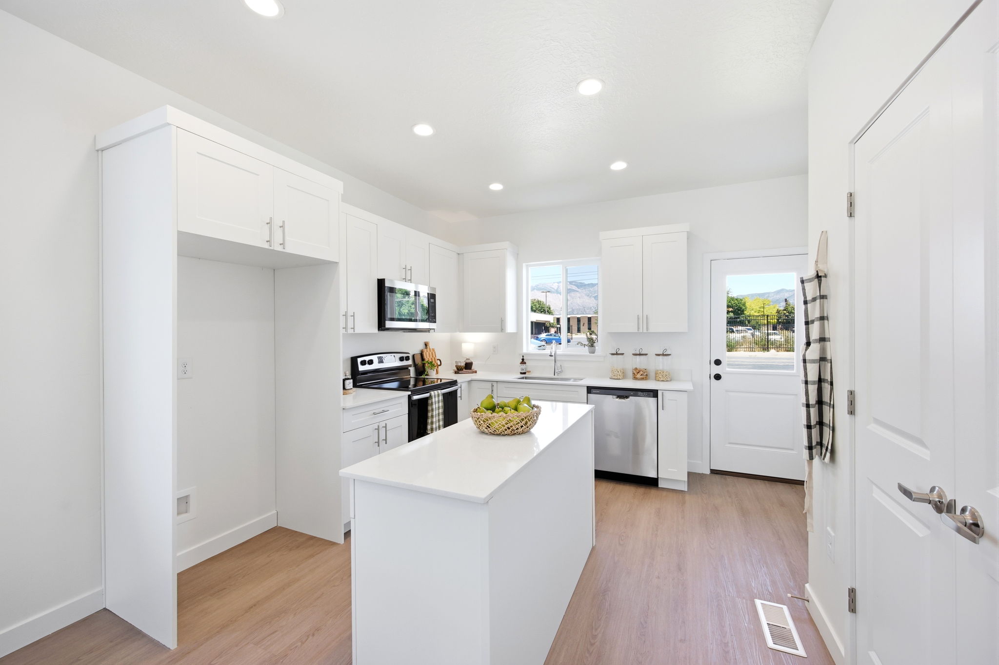 Contemporary kitchen featuring a central island, white cabinetry with brushed nickel hardware, stainless steel appliances, and light wood-finish flooring