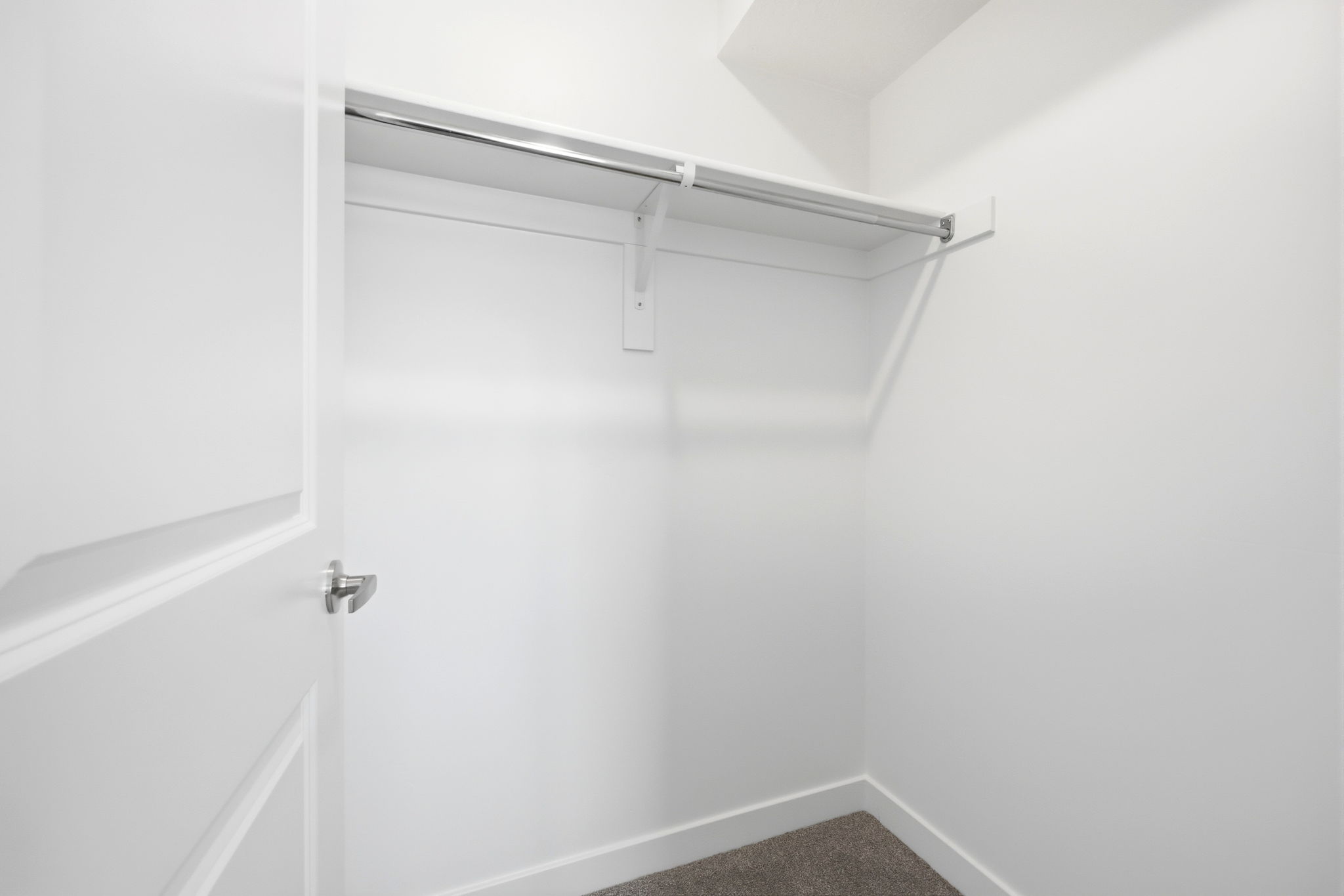 Spacious closet featuring a white door, white walls, and a single clothing rod with an upper shelf
