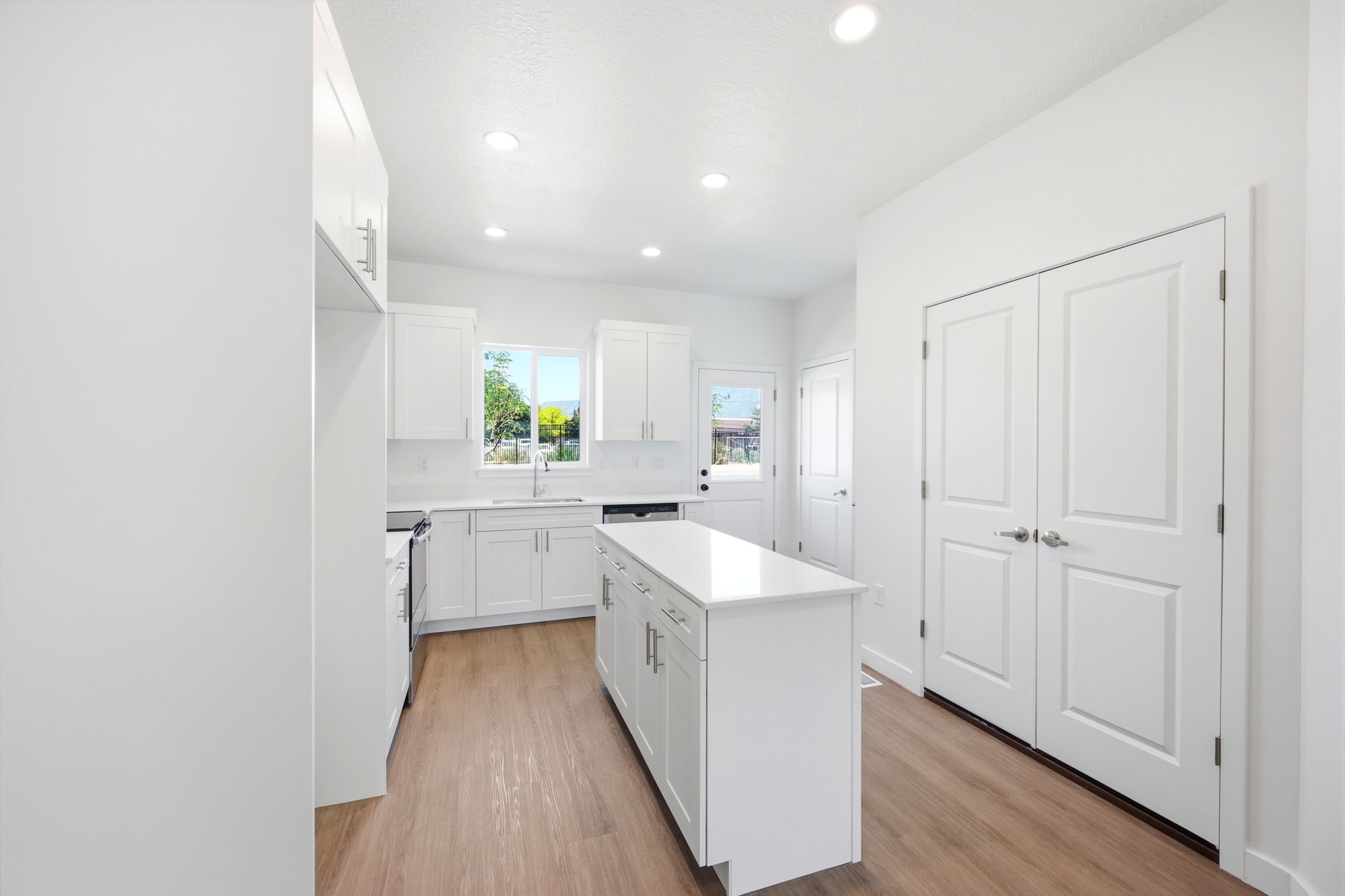 Bright kitchen featuring white cabinetry, a center island with a white countertop, wood-finish flooring, recessed lighting, and a double-door pantry