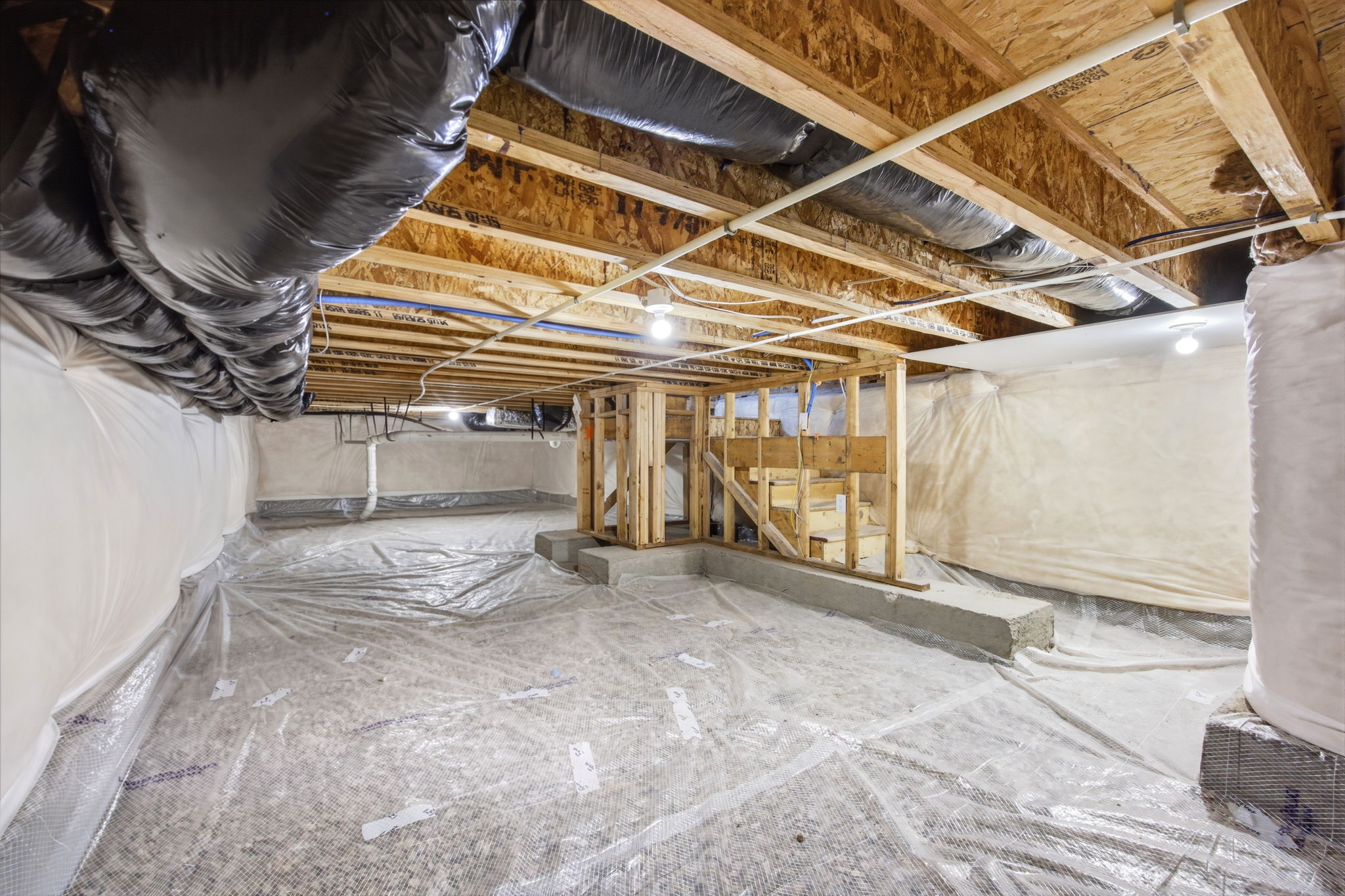 Unfinished crawlspace featuring exposed wood joists and subflooring, insulated walls and a partial wood-framed structure