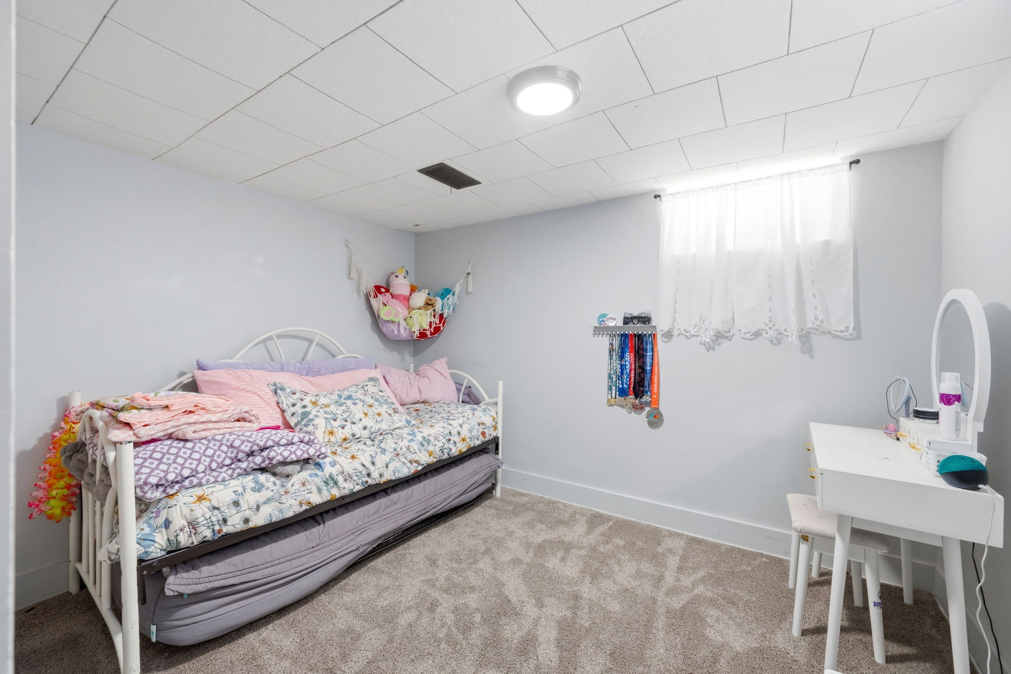 Carpeted room featuring a drop ceiling with recessed lighting, light-toned walls, and a window with white curtains