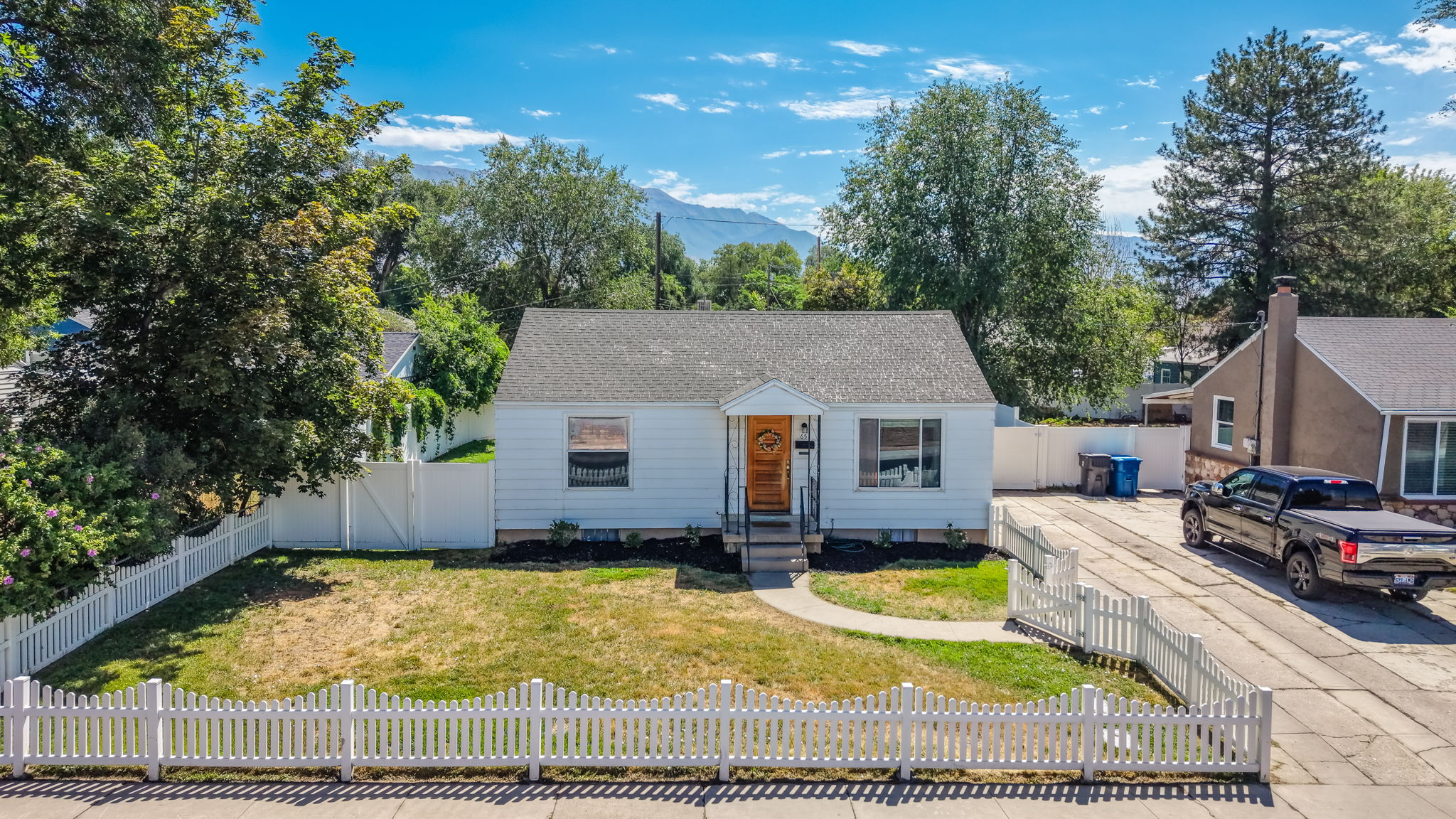 Charming single-story residence featuring a white picket fence, white siding, and a wooden front door