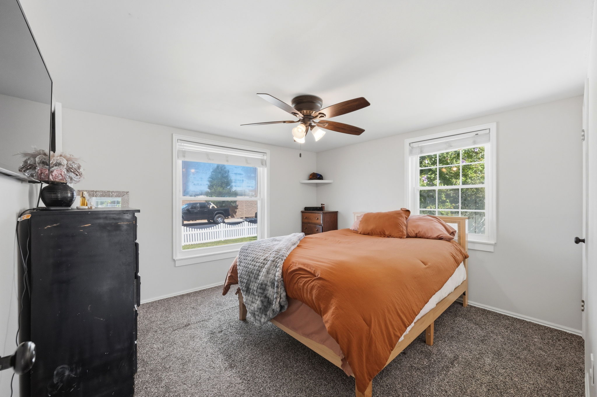 Carpeted room with a ceiling fan featuring a light fixture, two windows with white trim, and light gray walls