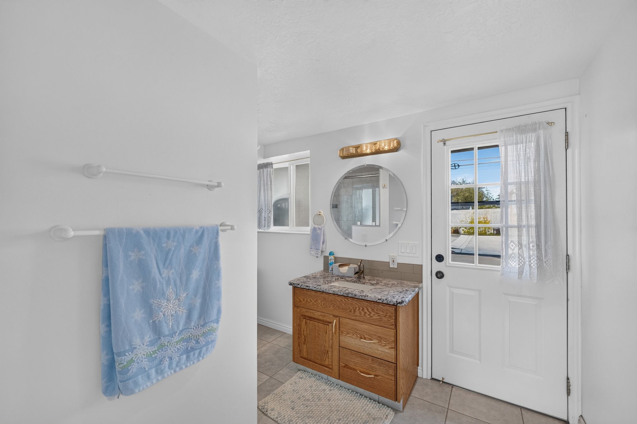 Bathroom vanity featuring a wood-finish cabinet, speckled countertop, and a circular wall-mounted mirror