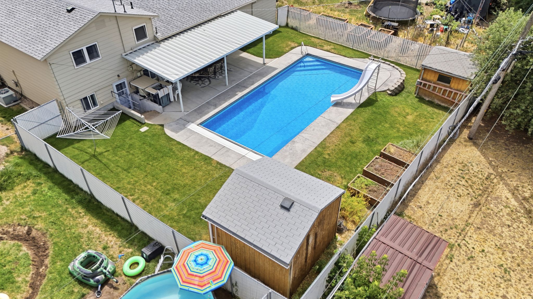 Rear exterior featuring an inground swimming pool with slide, a covered patio, and a spacious fenced yard