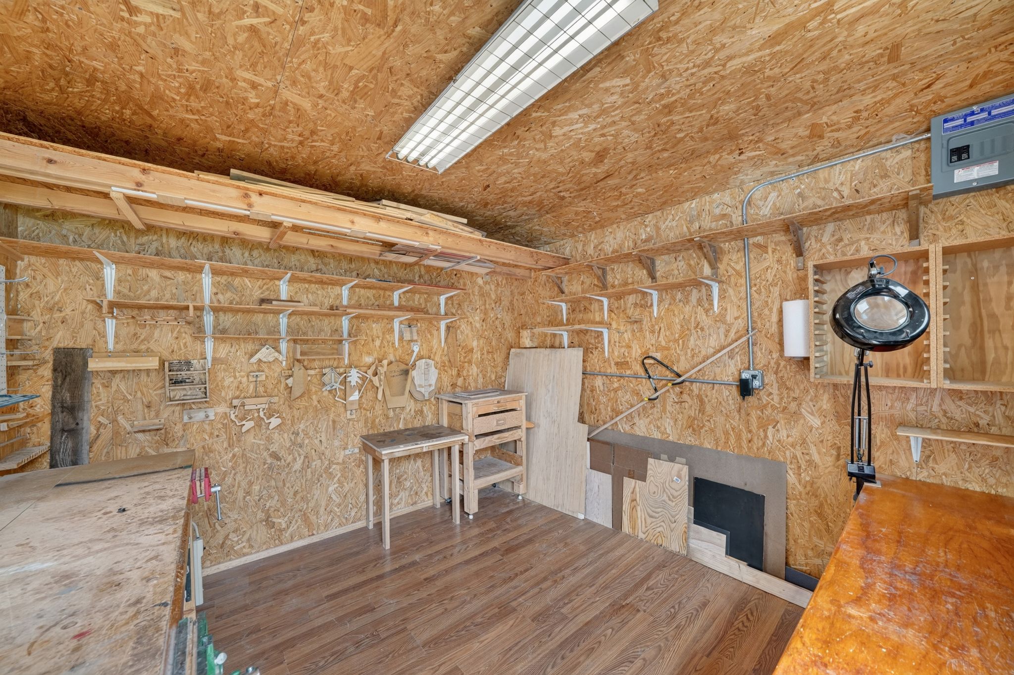 Utility room with wood-finish flooring, exposed OSB walls, extensive built-in shelving, and overhead fluorescent lighting